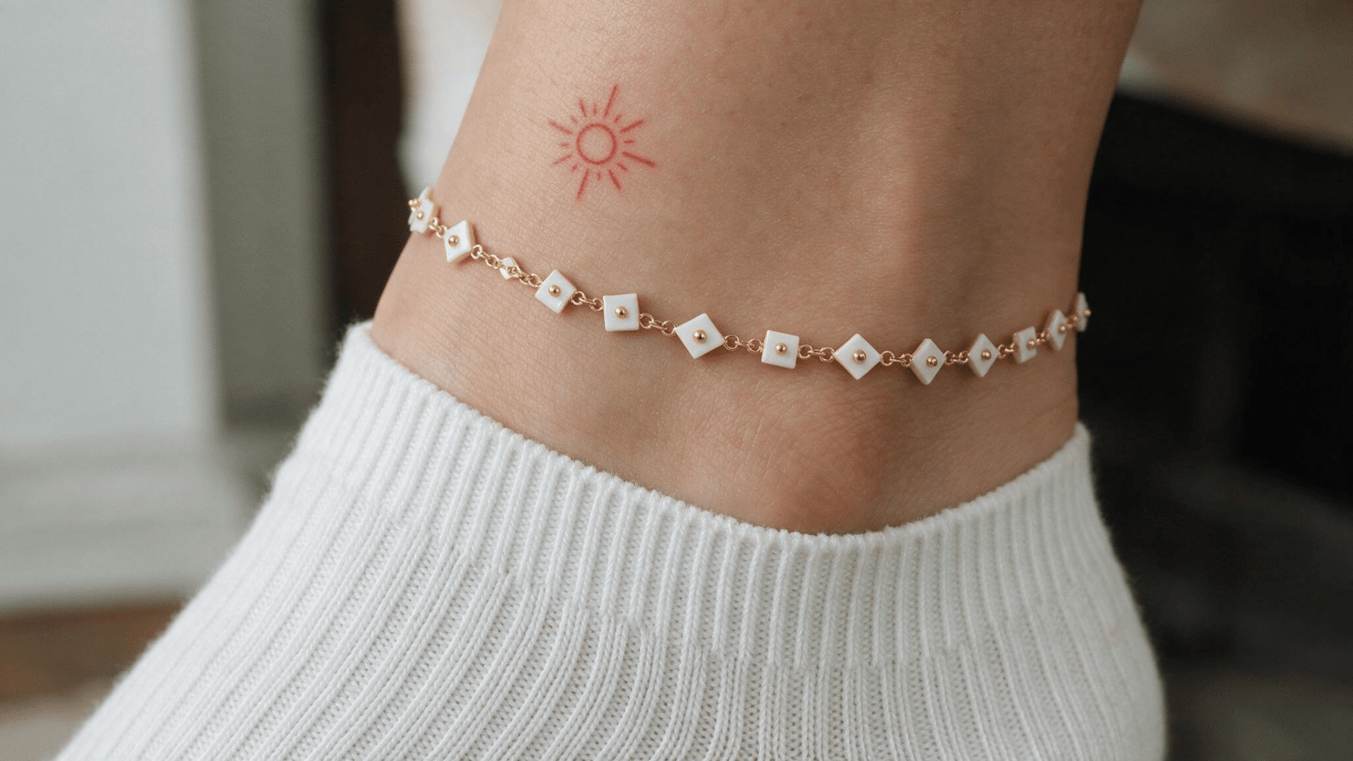 small red sun tattoo above a delicate gold and white anklet with a white ribbed sock.