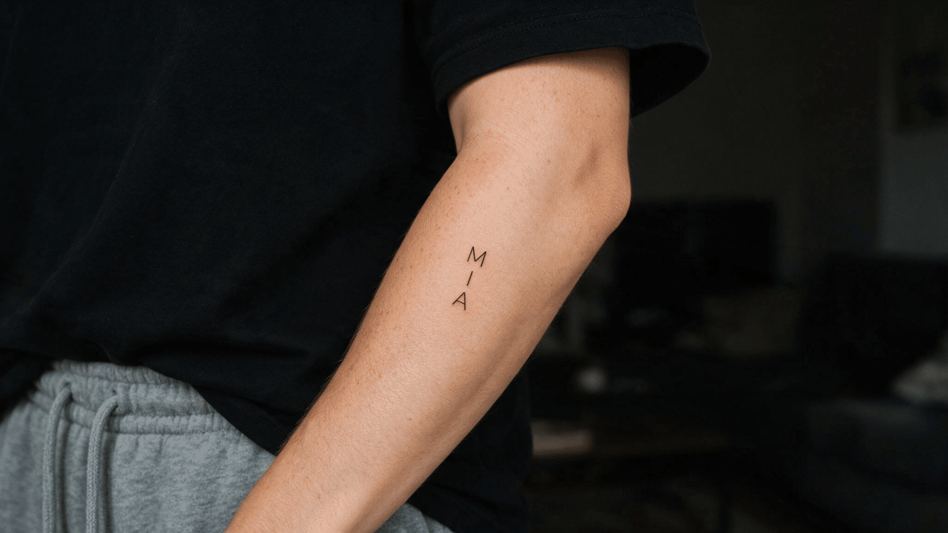 small vertical name tattoo reading “MIA” in fine black lettering on the inner forearm.