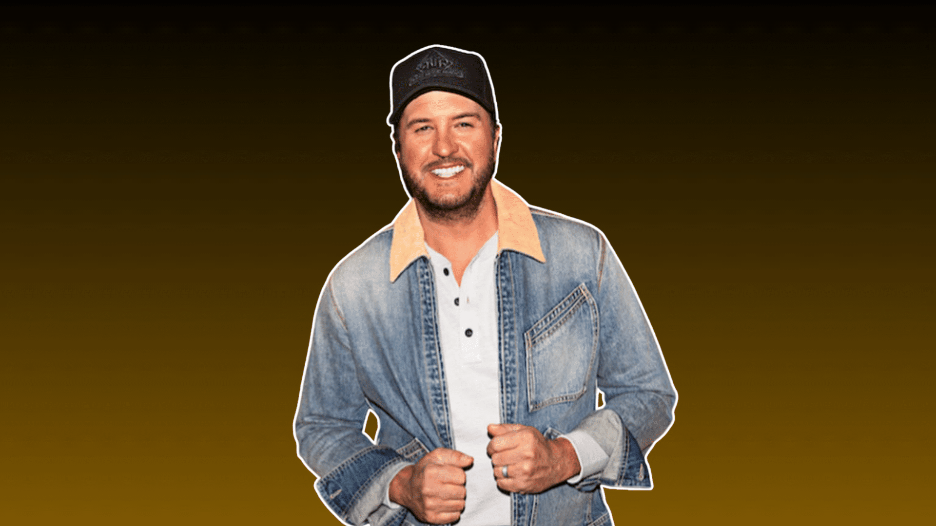 smiling man wearing a black cap and denim jacket over a white shirt against a dark brown background