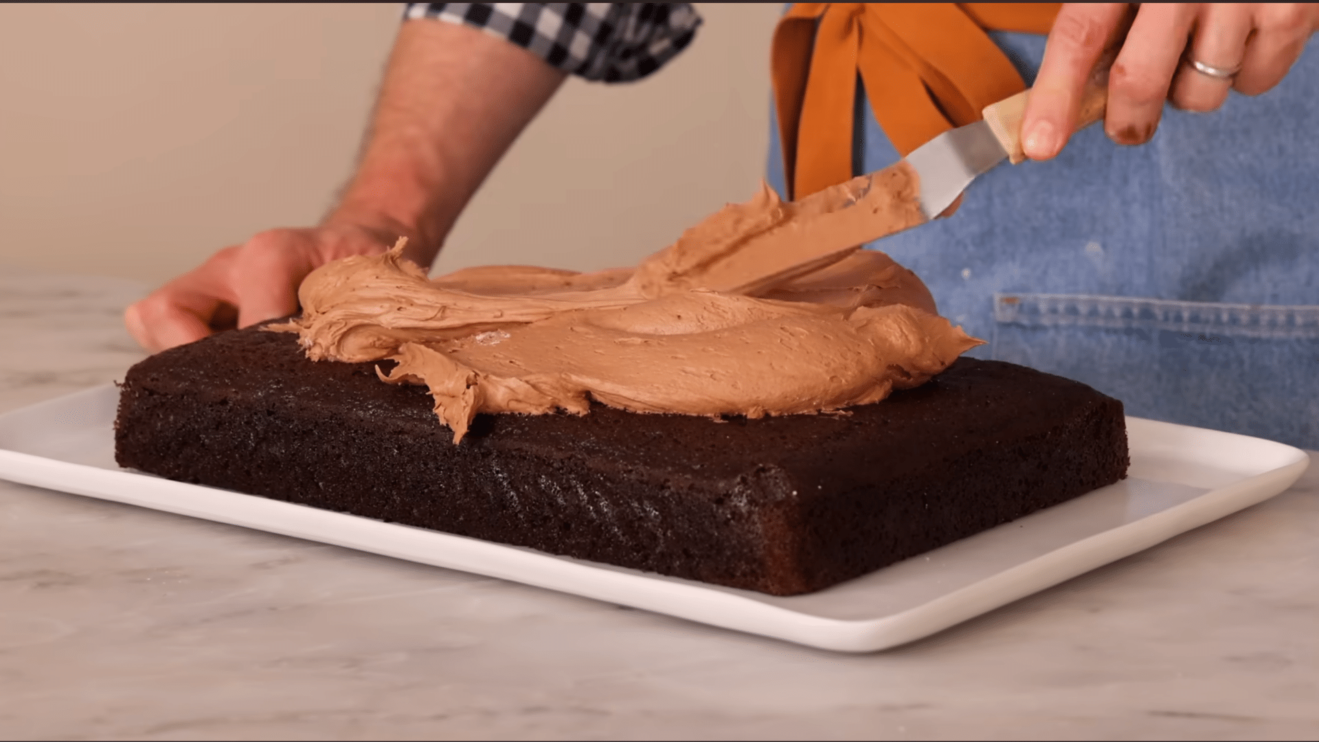spreading chocolate buttercream over cooled sheet cake with an offset spatula