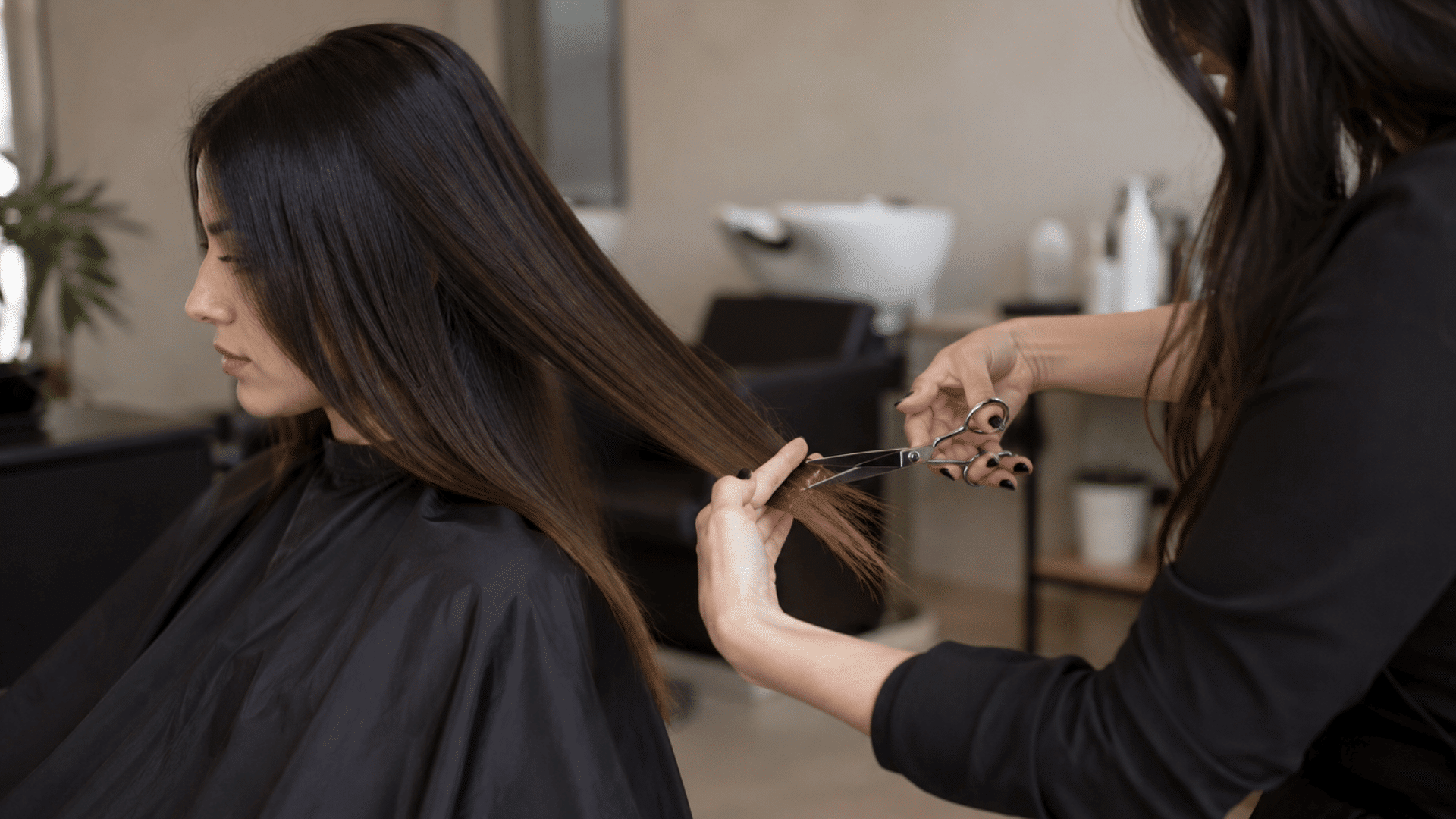 stylist trimming long straight hair with scissors while a client sits in a salon chair