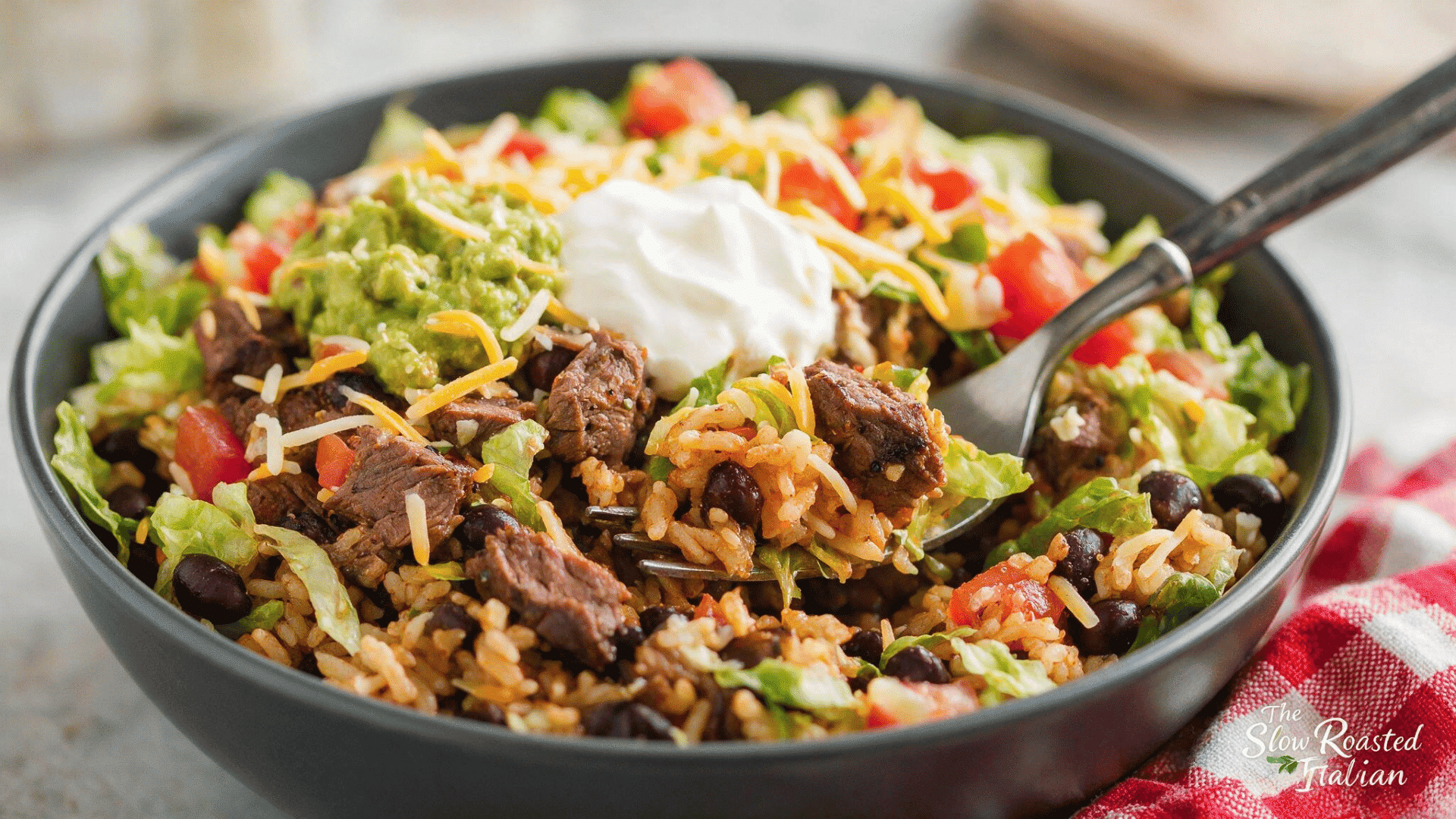 taco bell-style steak power bowl with seasoned rice, black beans, lettuce, tomatoes, cheese, guacamole, and sour cream.