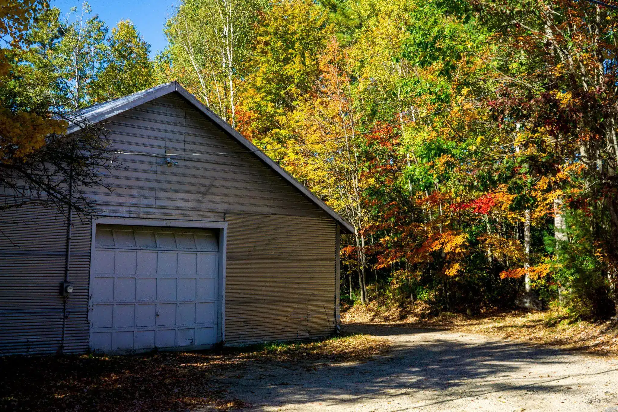 Gray barn against vibrant autumn trees and blue sky in a rural setting