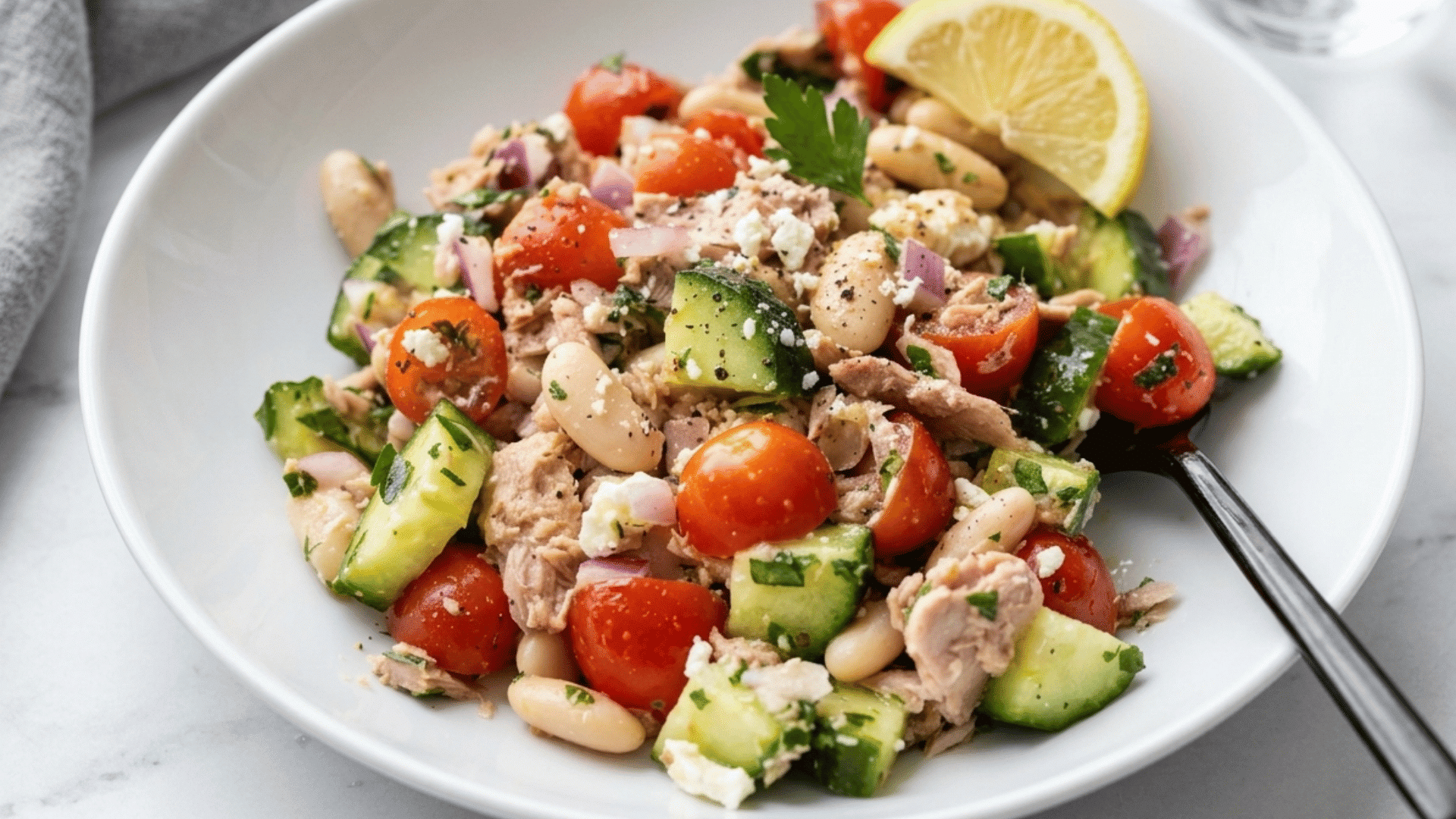 tuna and white bean salad with cucumber cherry tomatoes red onion feta, fresh herbs and a lemon wedge