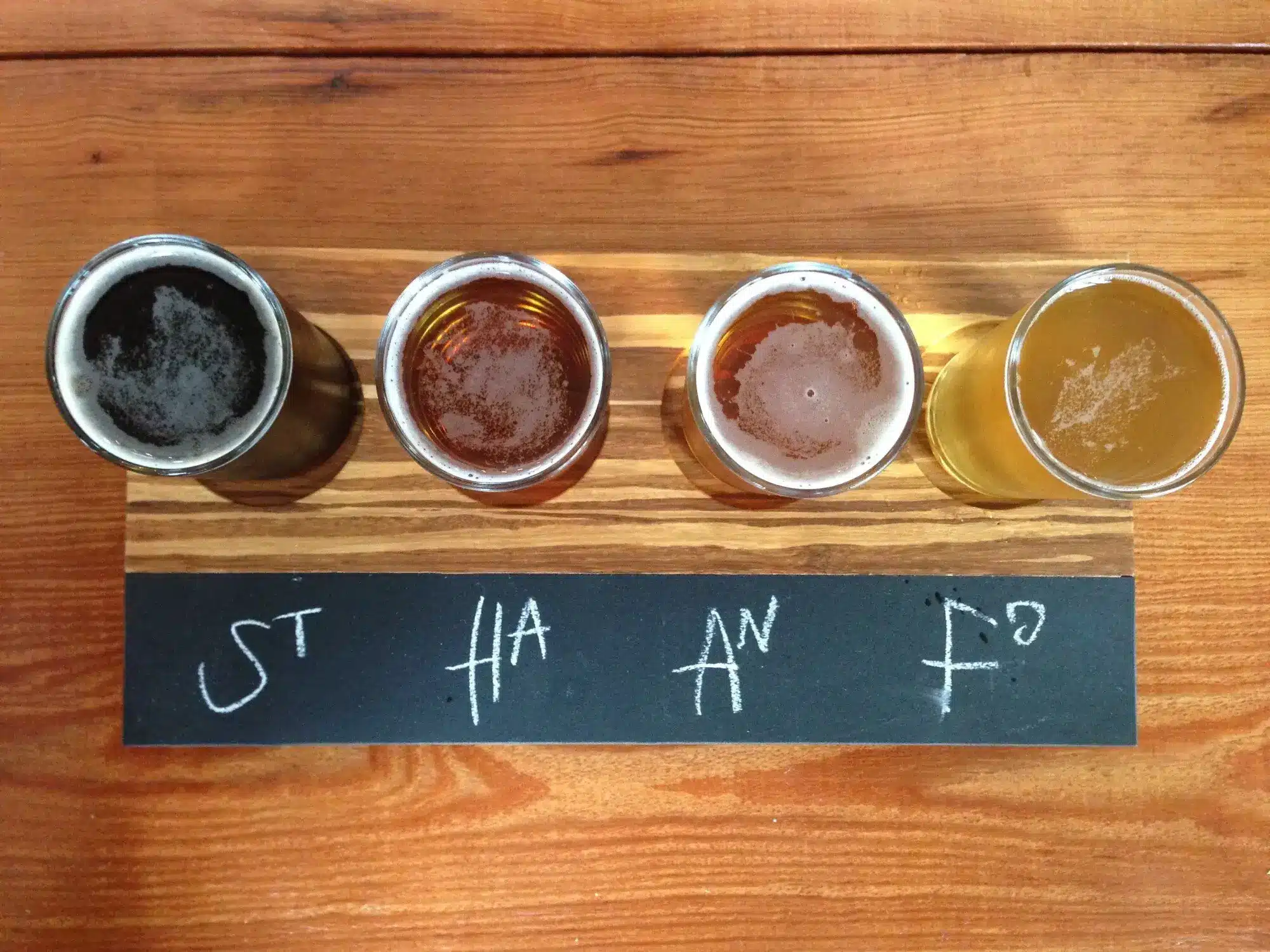 Four glasses of different craft beers on a wooden table with chalkboard labels