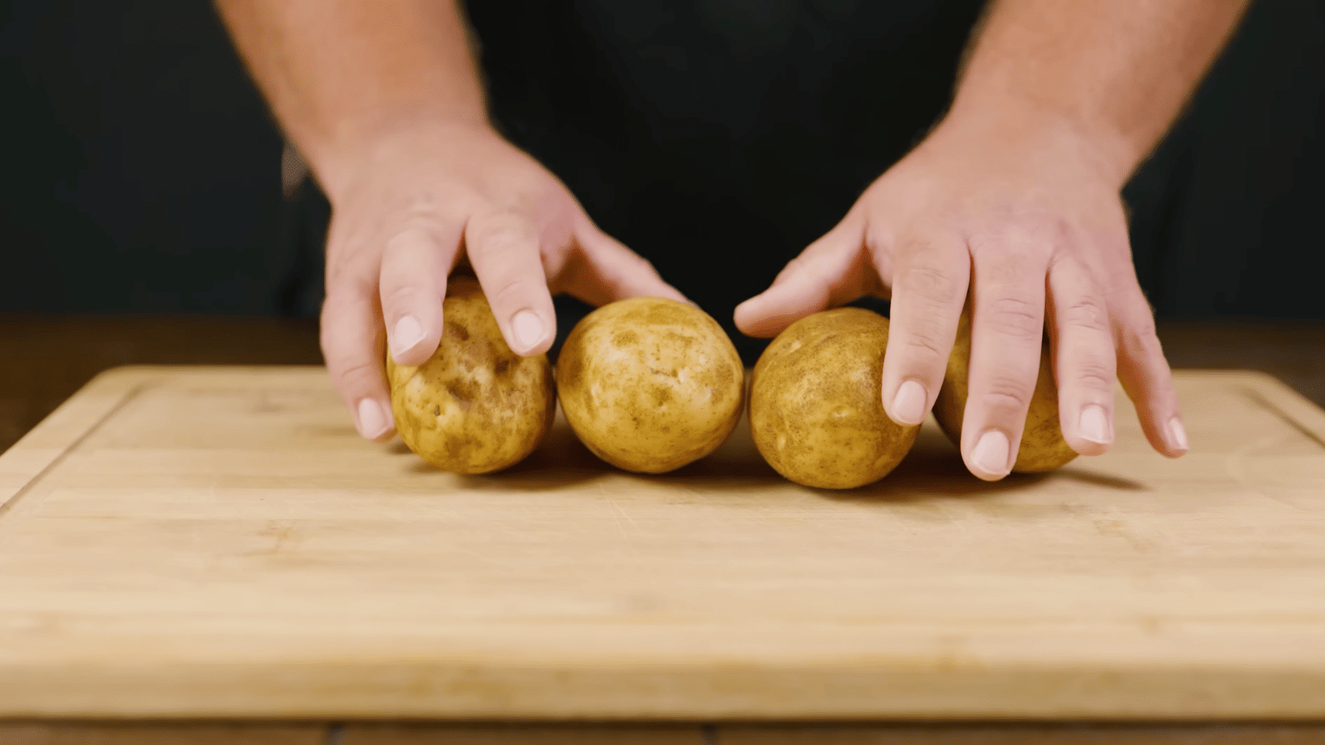 washed and peeled potatoes prepared on a kitchen counter beside a bowl of cold water