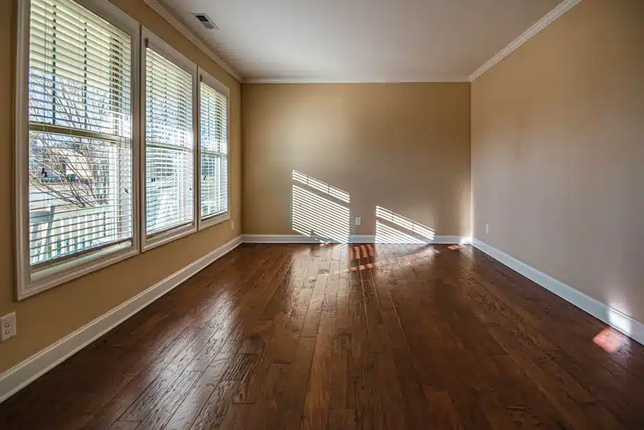 Empty room with hardwood floor, large windows, and beige walls in natural light