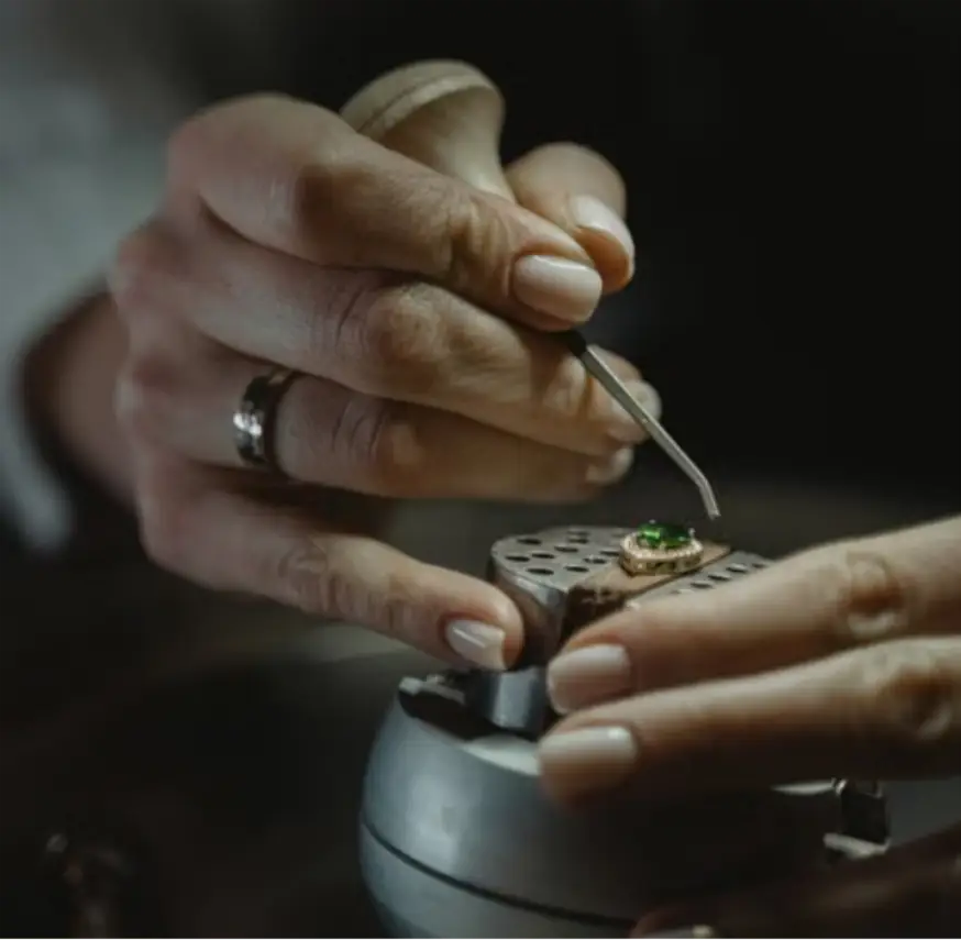 Jeweler setting green gemstone into ring using metal tool in dimly lit workshop