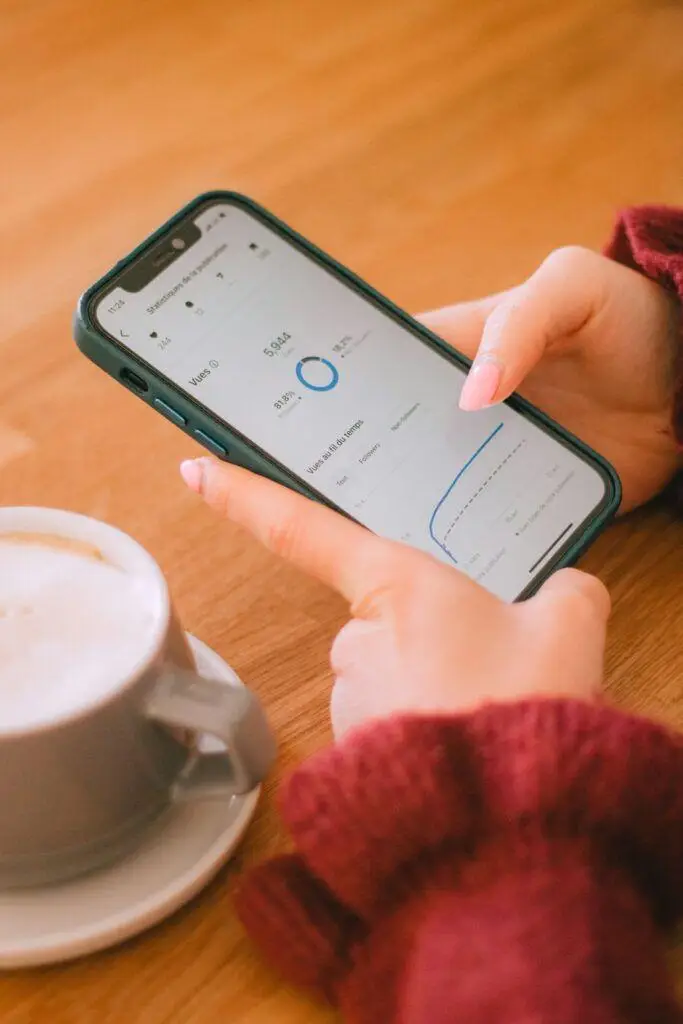 Person holding smartphone displaying analytics beside coffee cup on wooden table
