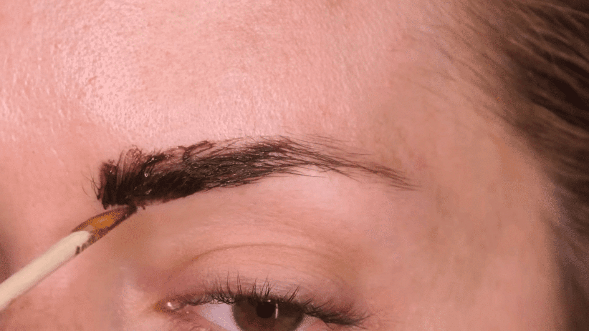 woman applying eyebrow tint with a small brush for defined darker brows