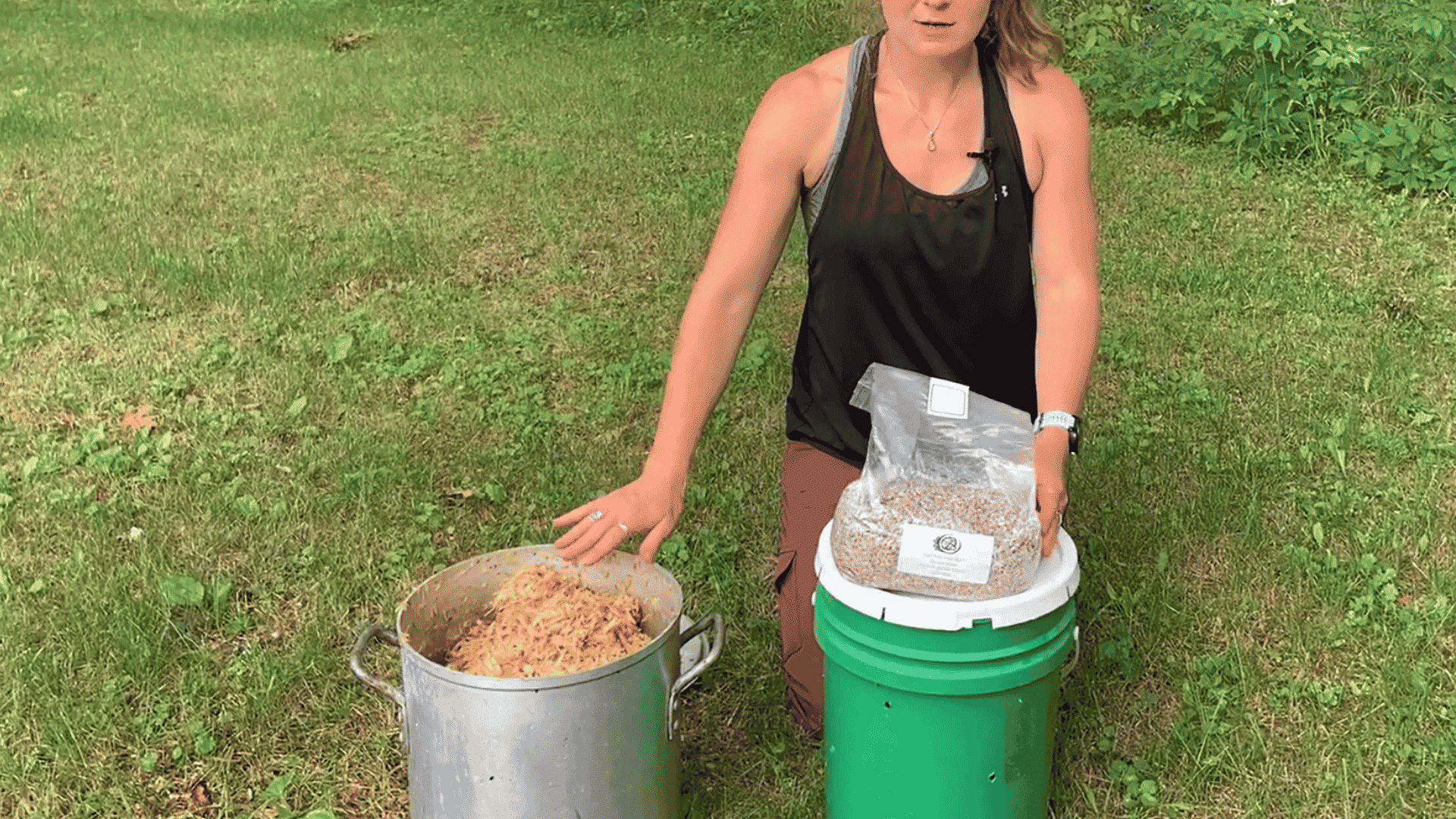 woman preparing to layer hydrated aspen shavings and oyster mushroom grain spawn inside a green growing bucket