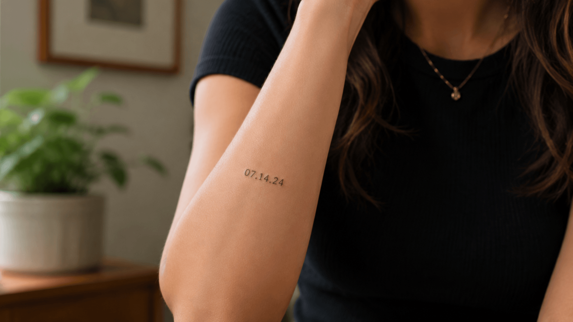 woman showing a small date tattoo on her inner forearm in a cozy indoor setting