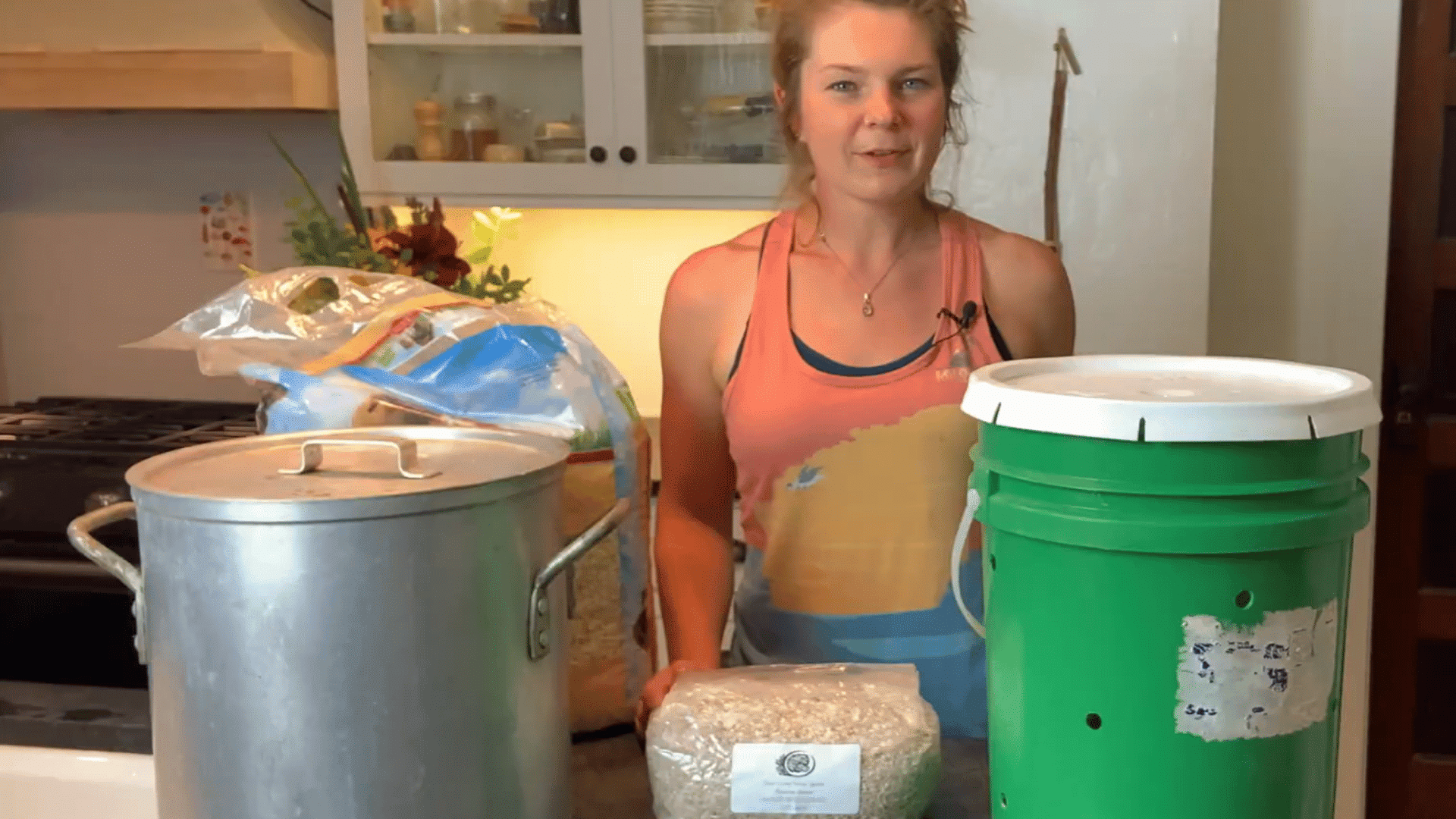 woman standing beside a green growing bucket large pot aspen shavings and oyster mushroom grain spawn