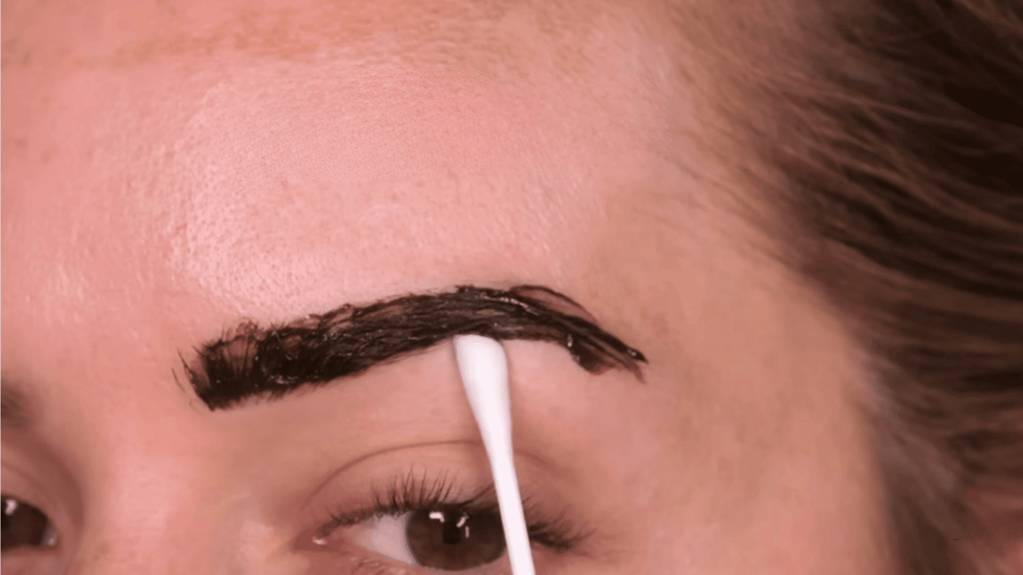 woman using a damp cotton bud to clean the edges of freshly applied eyebrow tint for a neat finish