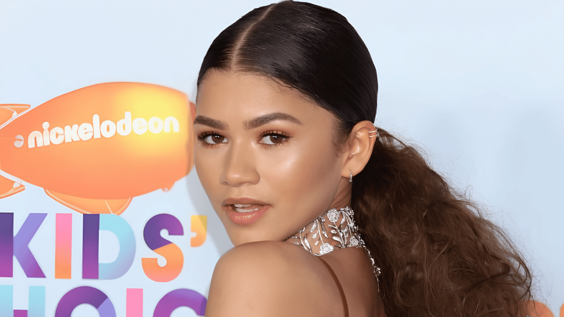 woman wearing a sleek center part ponytail with voluminous curls and jeweled earrings at a formal event