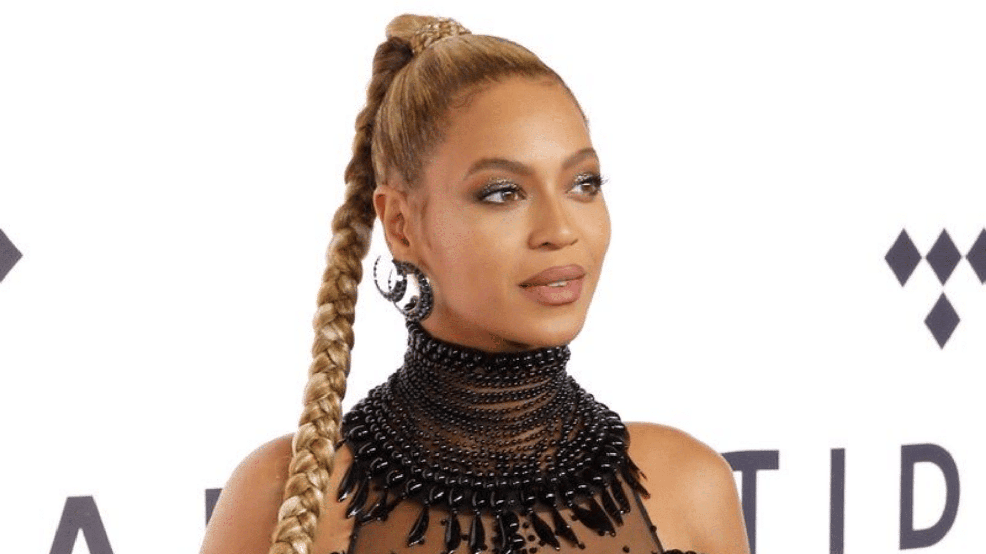 woman wearing a sleek high braided ponytail with statement earrings and black beaded neckline at a formal event