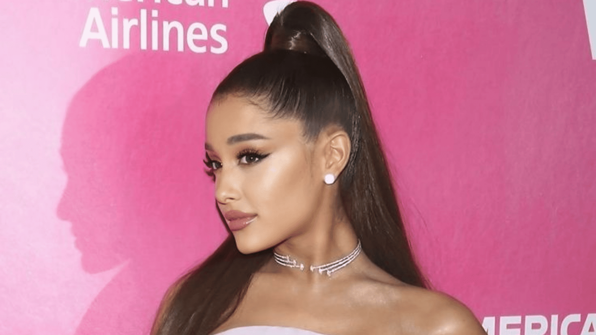woman wearing a sleek high ponytail with long straight hair diamond choker and stud earrings against a pink backdrop