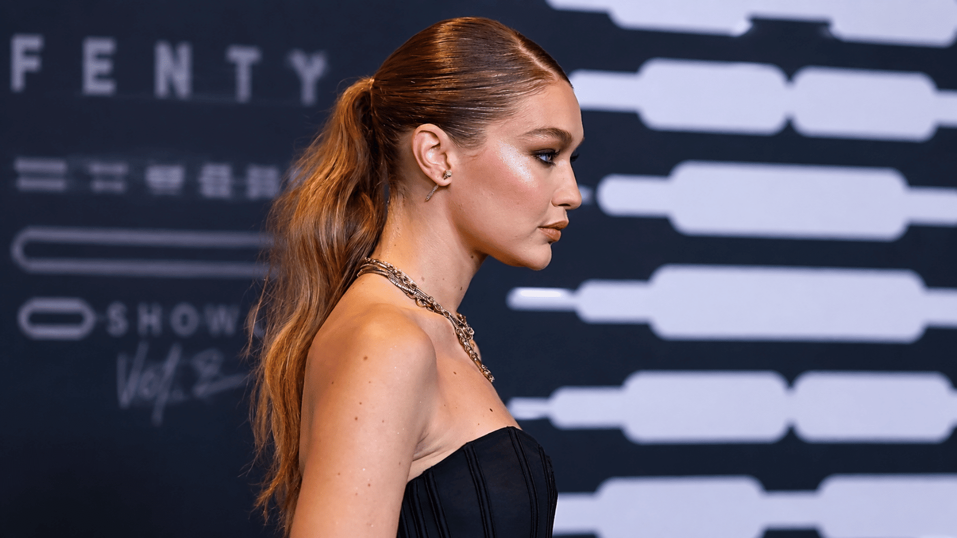 woman wearing a sleek low wavy ponytail with center part black strapless dress gold necklace and earrings