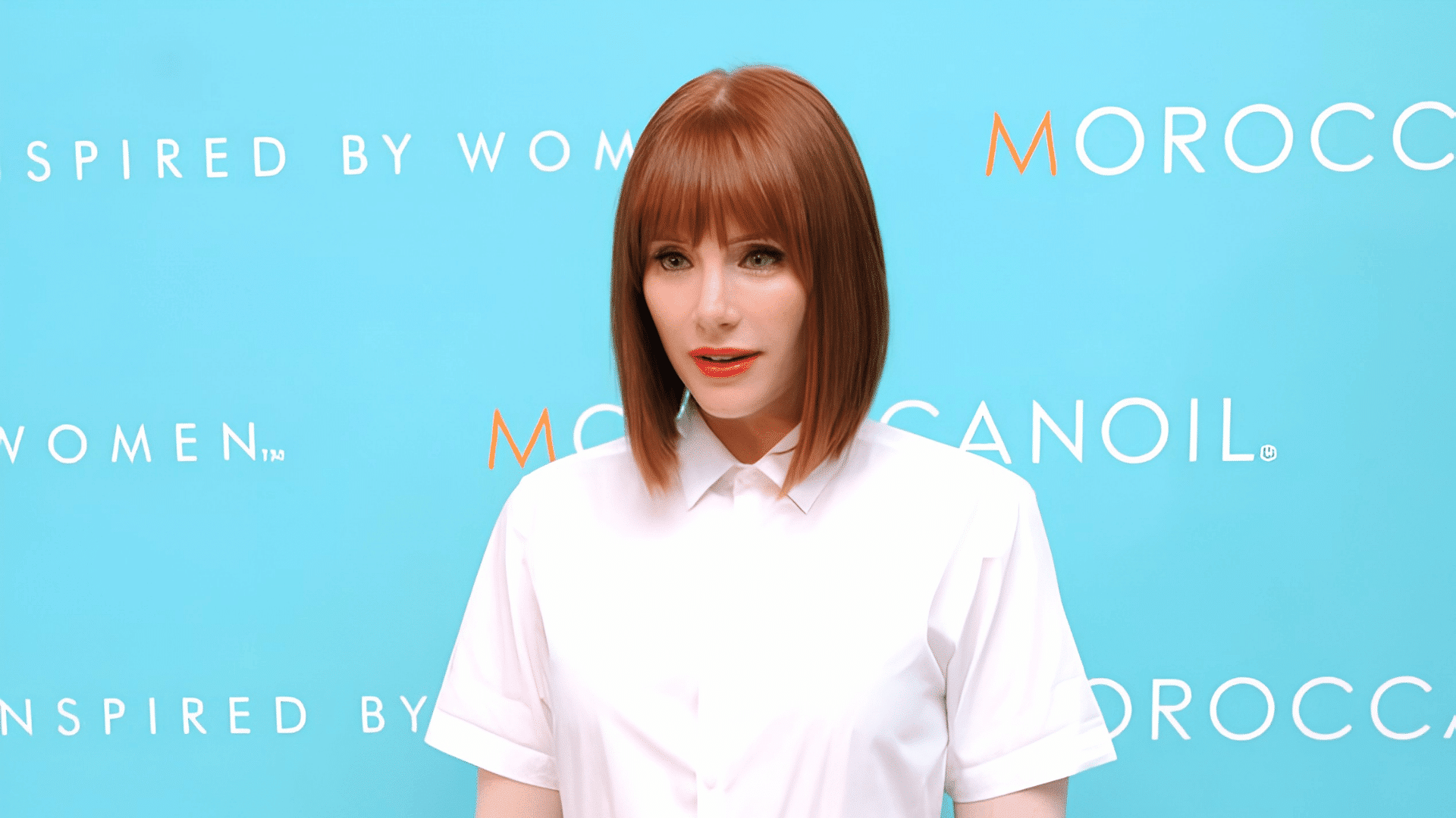 woman with an angled layered bob featuring sleek auburn hair and full bangs wearing a crisp white collared top