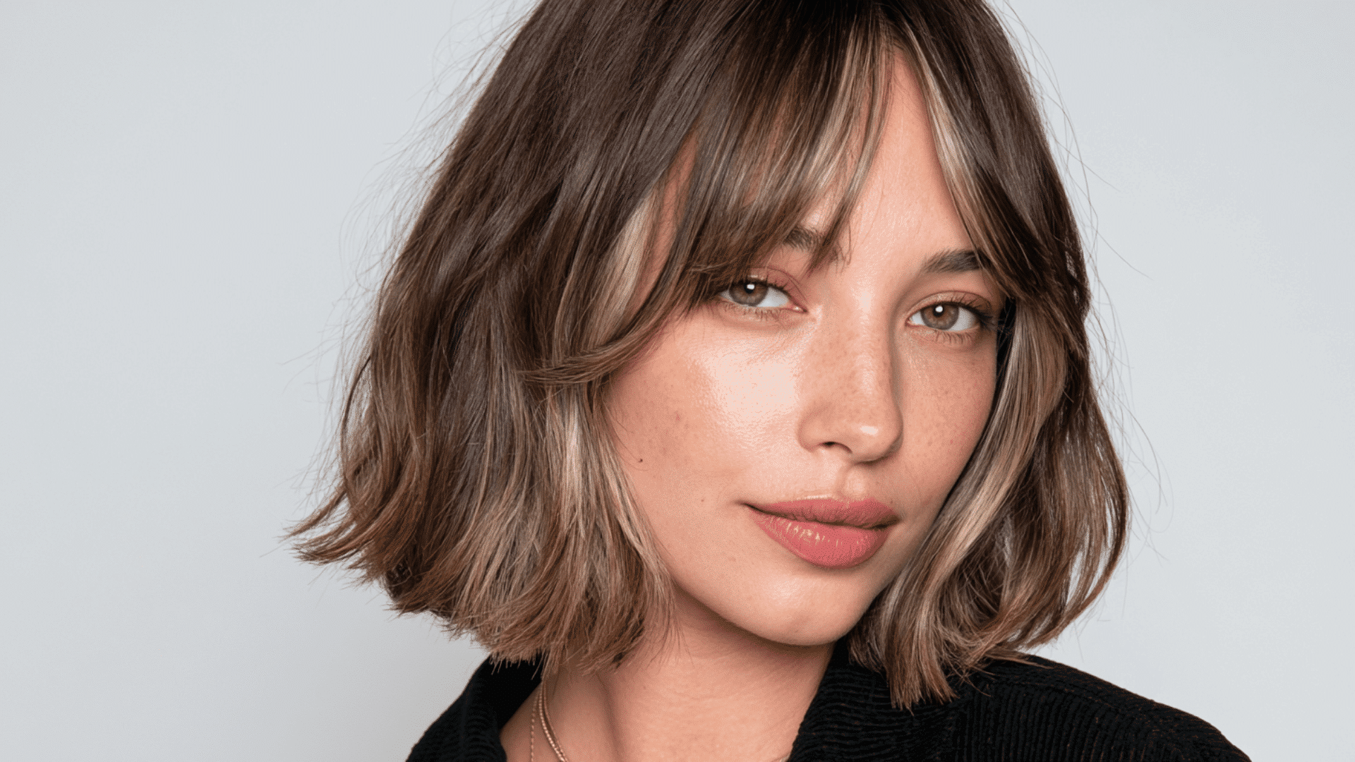 woman with beige blonde money piece highlights on a softly waved jaw length brunette bob