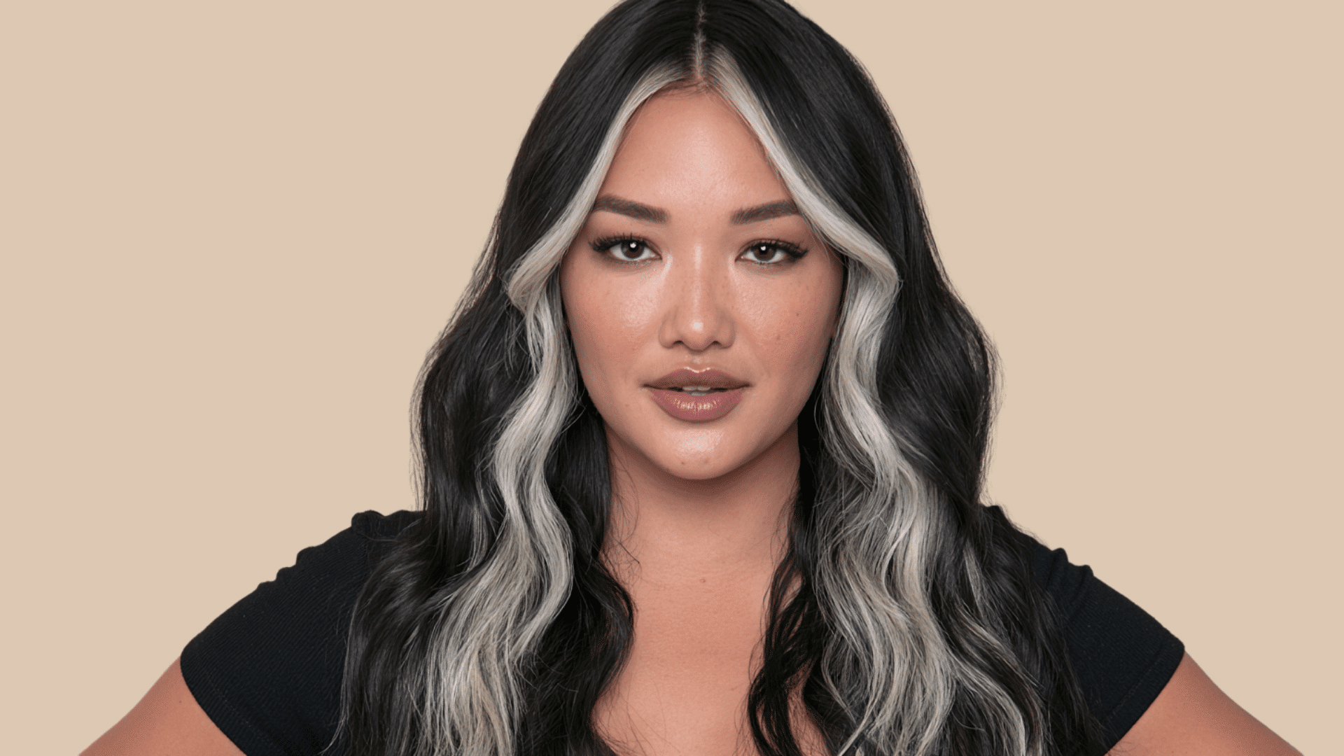 woman with bold silver money piece highlights framing long wavy black hair against a neutral background