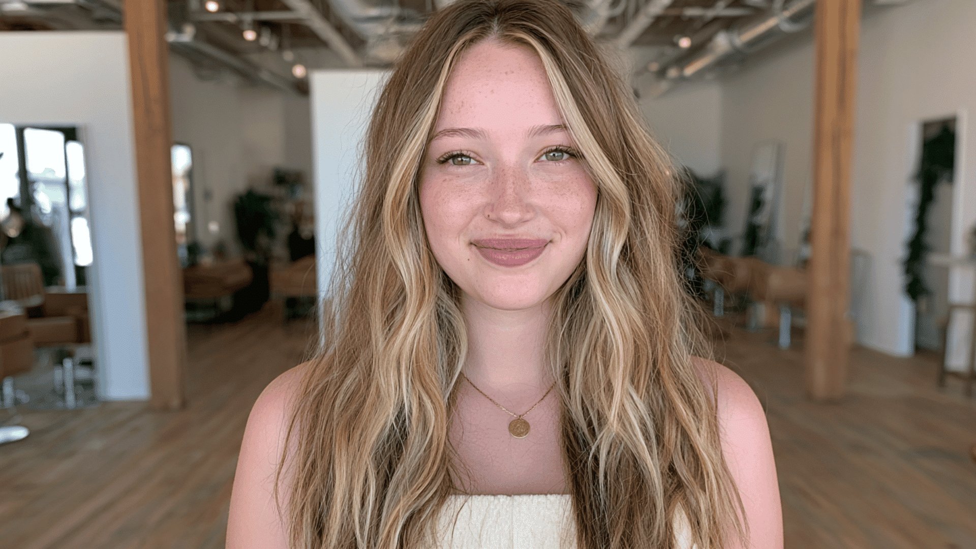 woman with butter blonde money piece highlights framing long wavy dark blonde hair in a modern salon