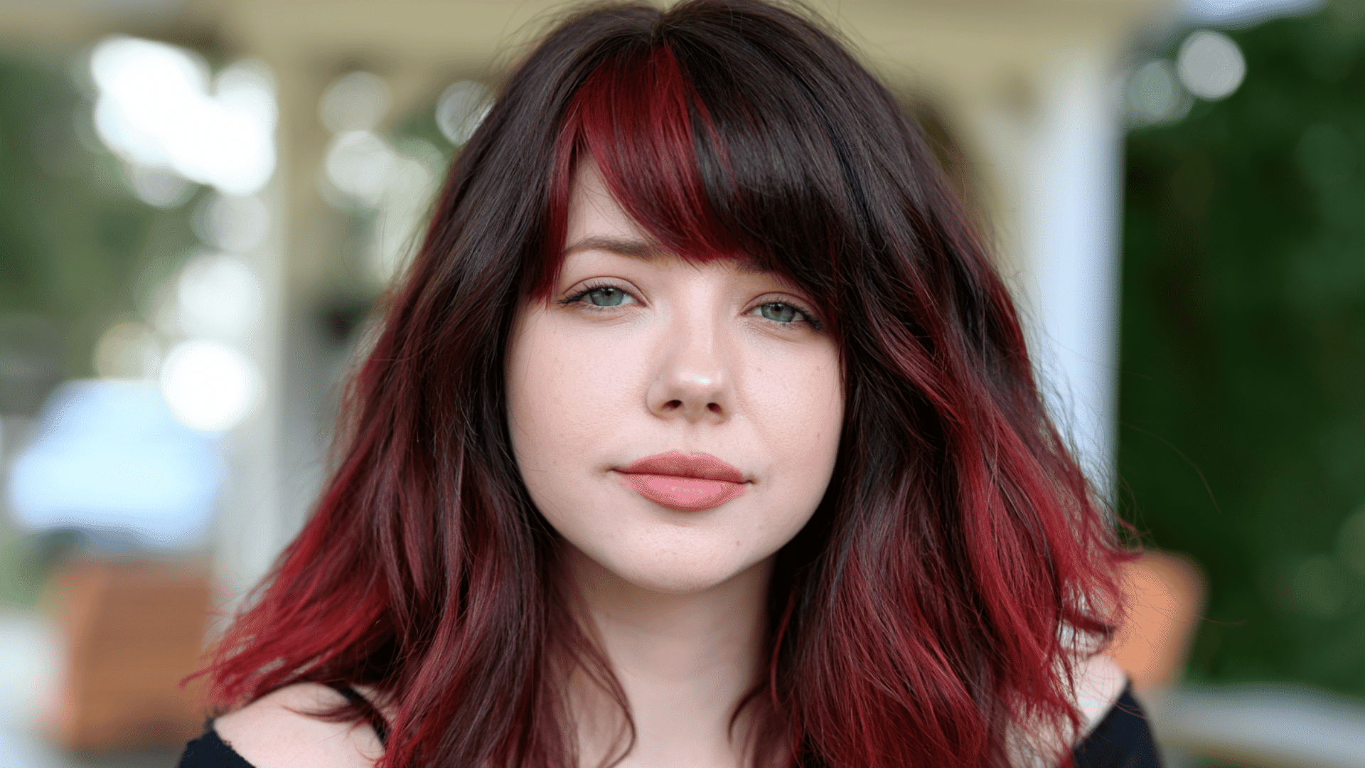 woman with cherry red money piece streaks blended through long wavy dark auburn hair