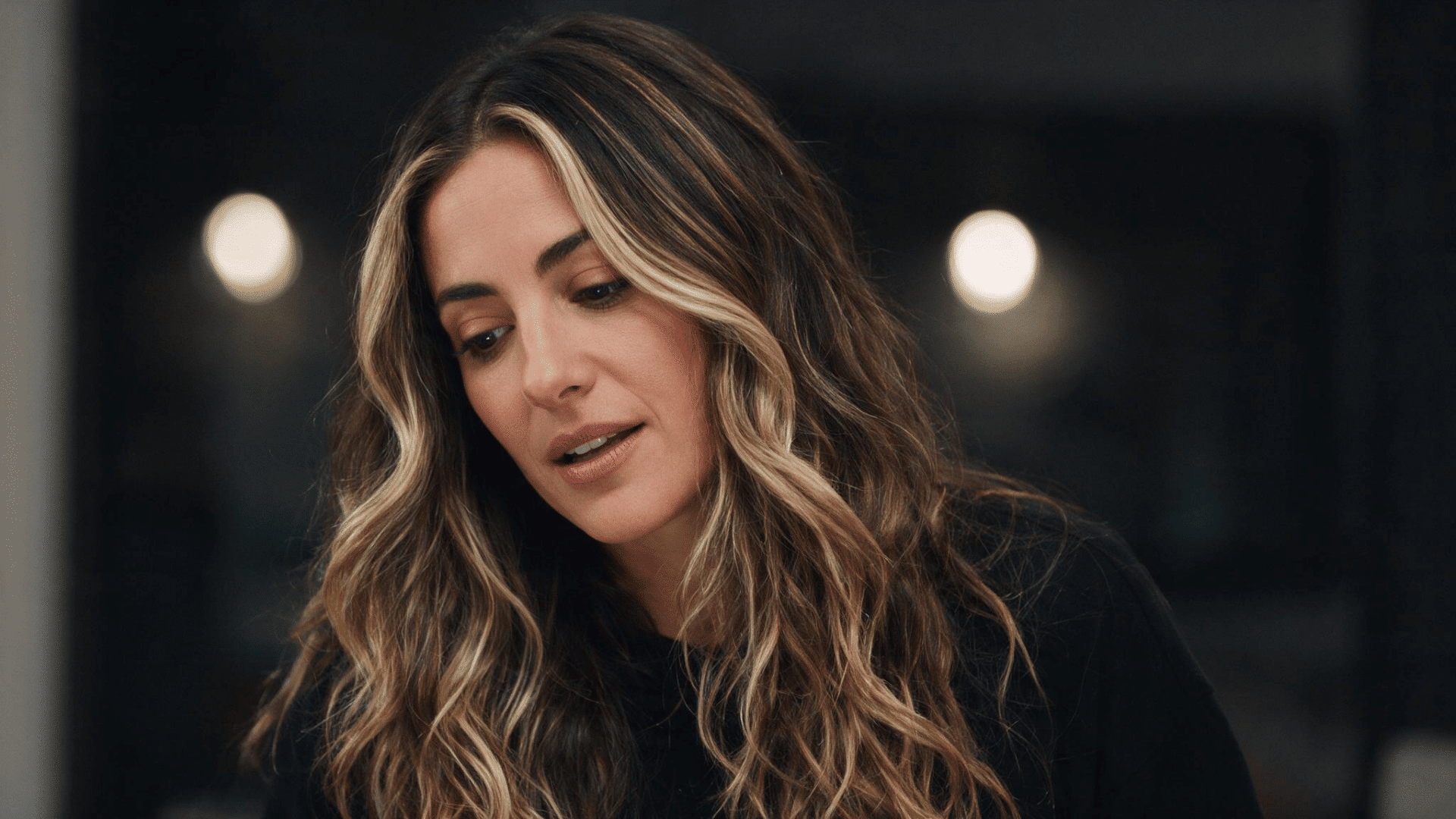 Woman with dark wavy hair featuring blonde chunky highlights around the face.