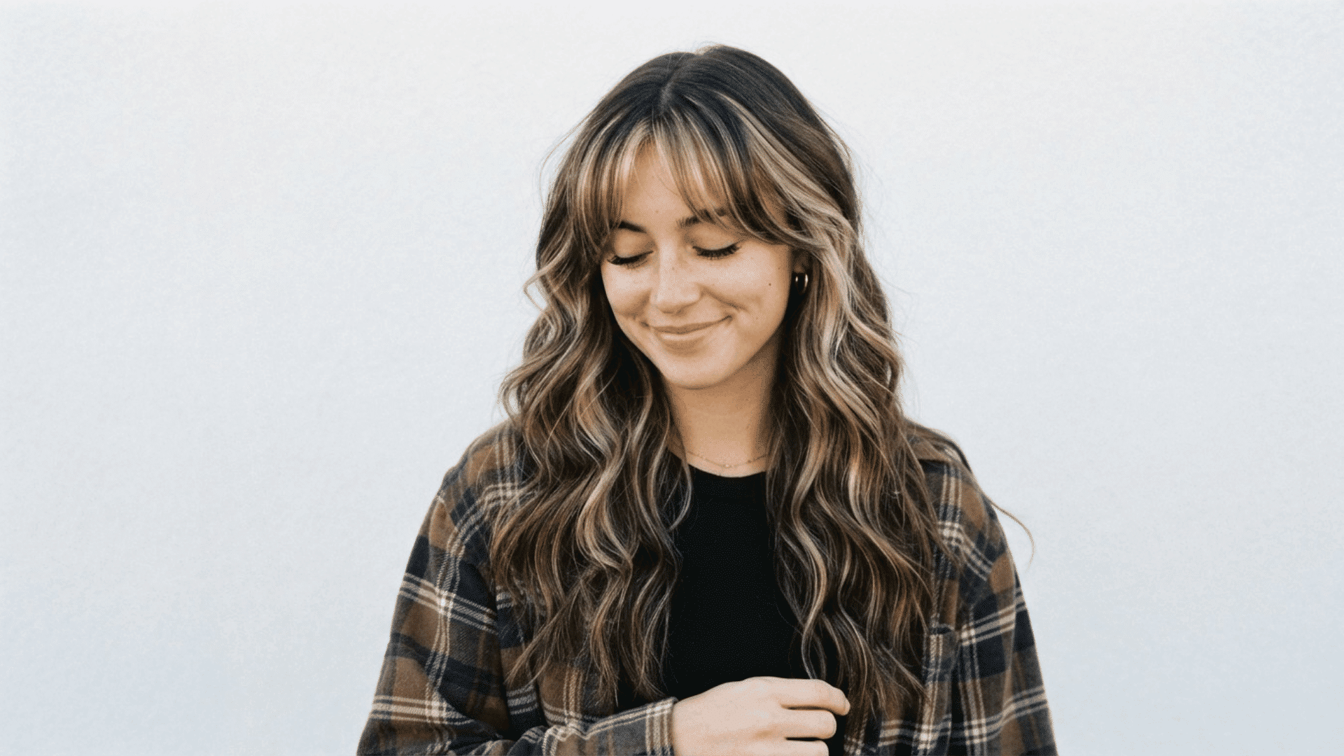 Woman with dark wavy hair featuring blonde chunky highlights and face-framing lighter strands.