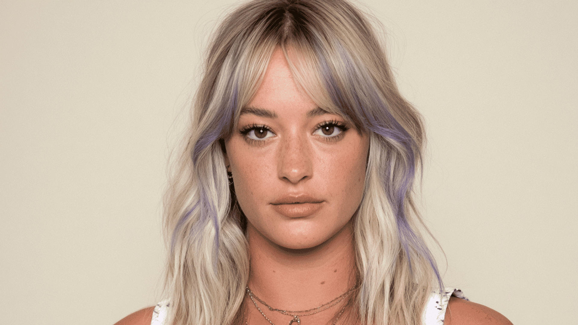 woman with lavender money piece highlights and curtain bangs on soft wavy blonde hair