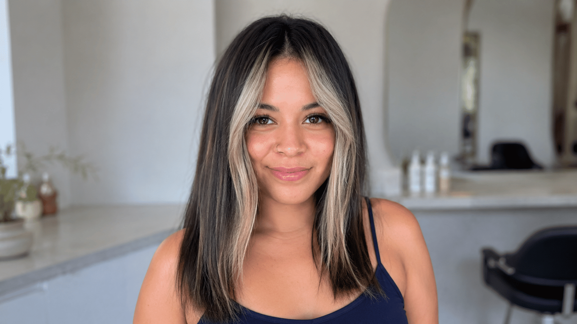 woman with straight black hair and ash blonde face framing highlights wearing a navy blue strappy top