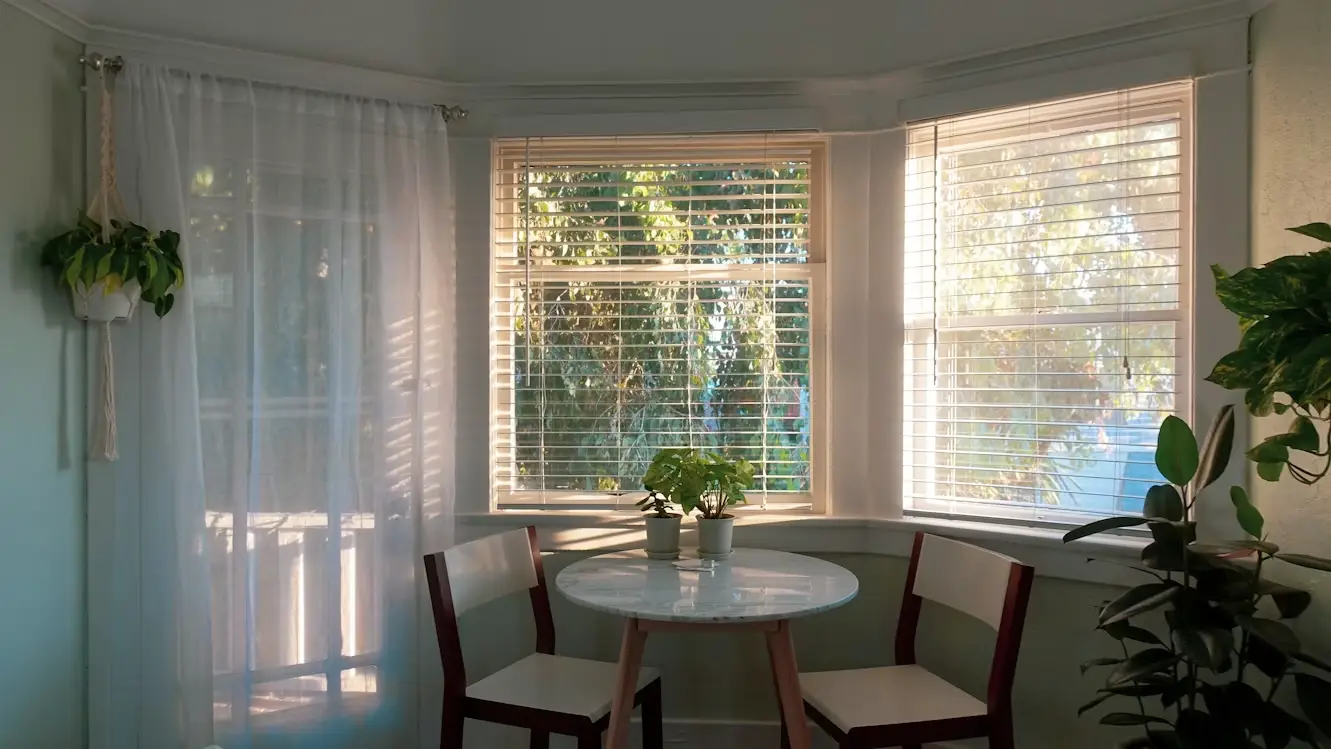 Cozy dining area with round table and chairs, sunlight streaming through large windows