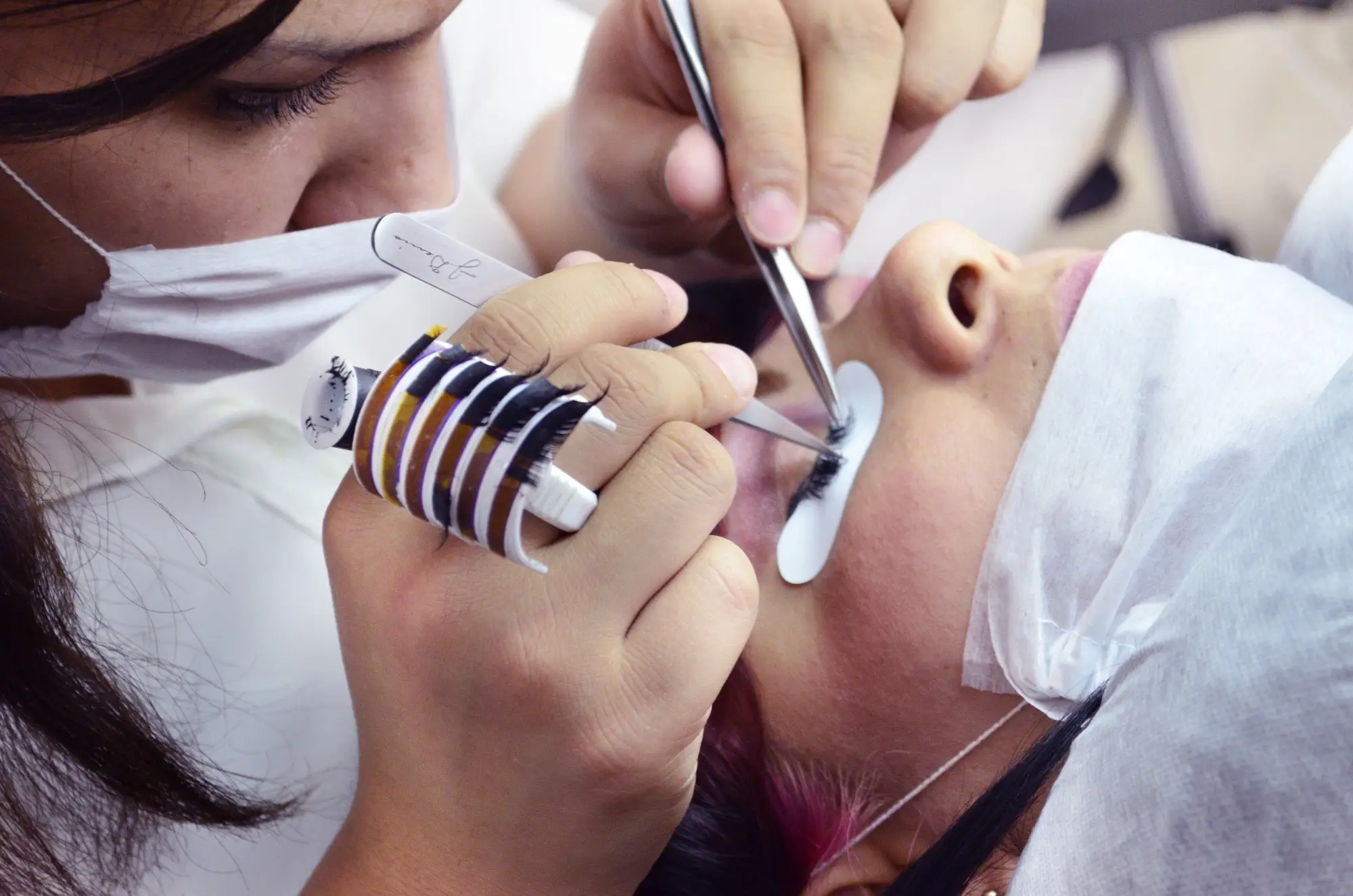 Close-up of a person applying false eyelashes with tweezers in a beauty salon