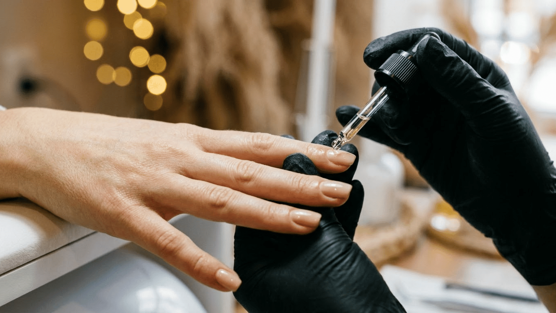 a technician applying cuticle oil to a client natural nail using a brush applicator in a spa setting