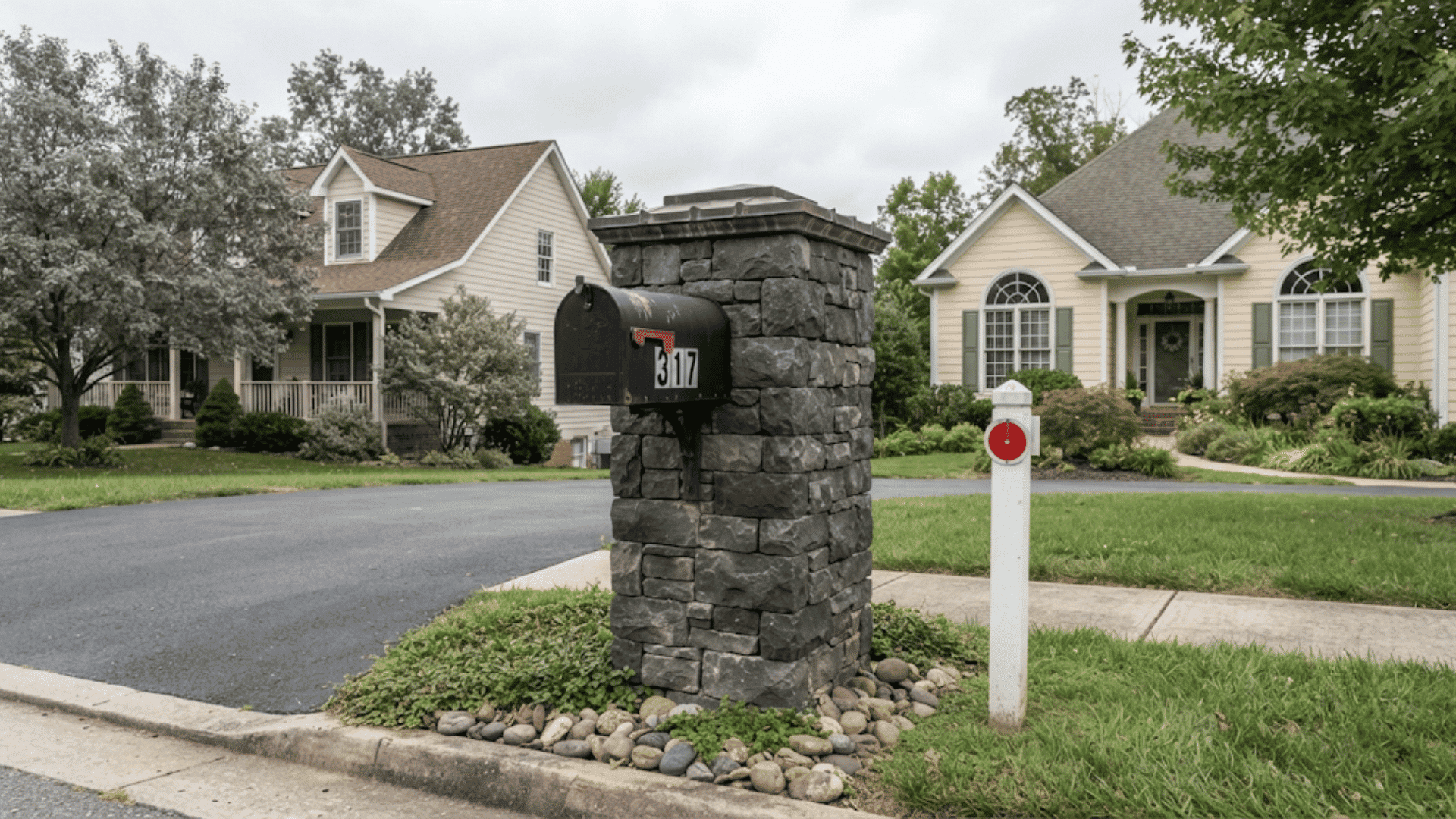 black brick mailbox with address numbers beside a suburban driveway surrounded by lawn stones and neighboring homes