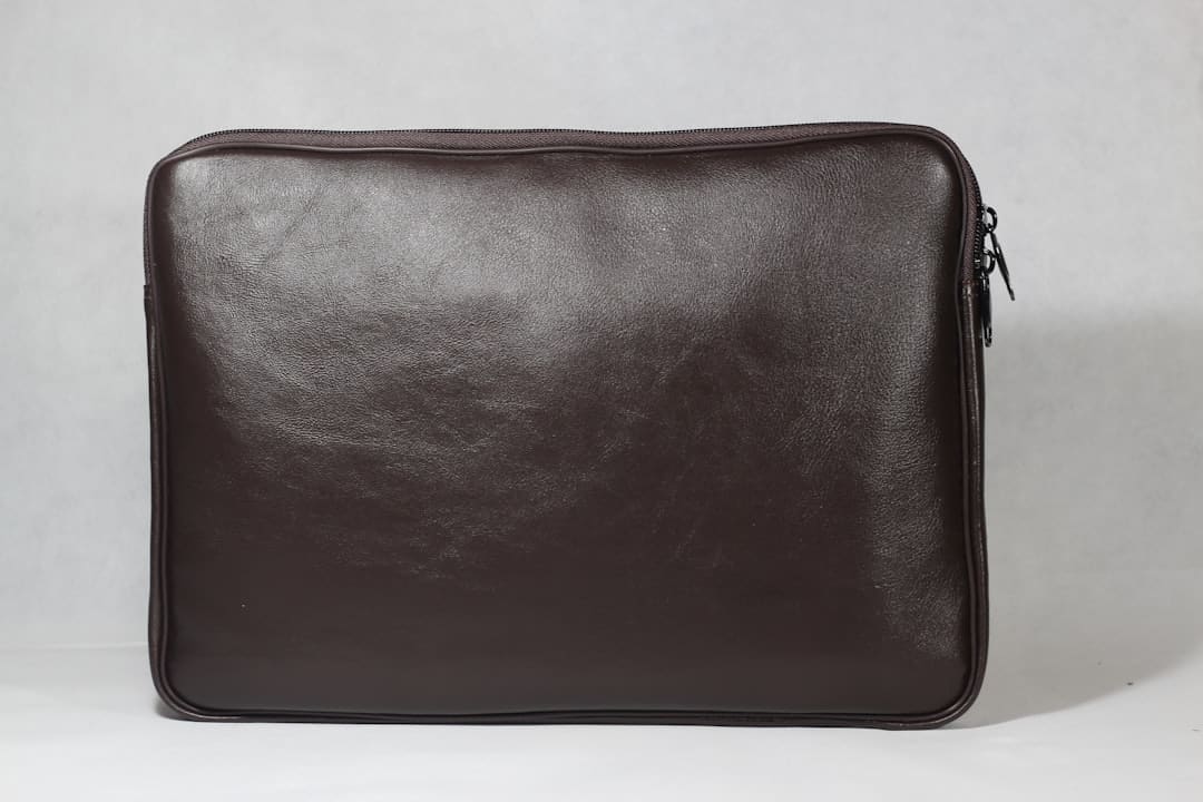 Dark brown leather laptop sleeve with a zipper on a plain white background