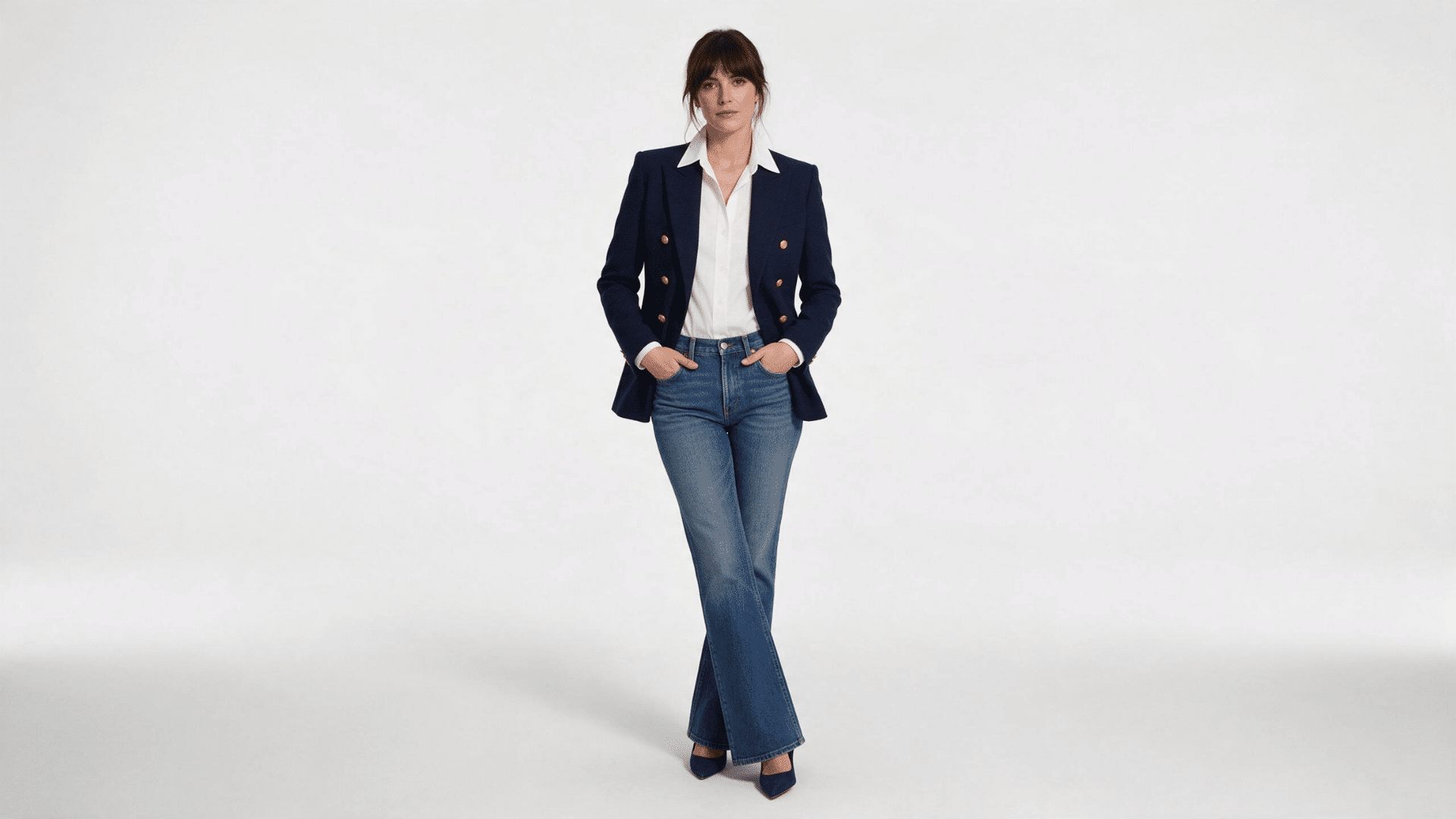 woman wearing a navy blazer white shirt and dark blue jeans with pointed heels against a white background