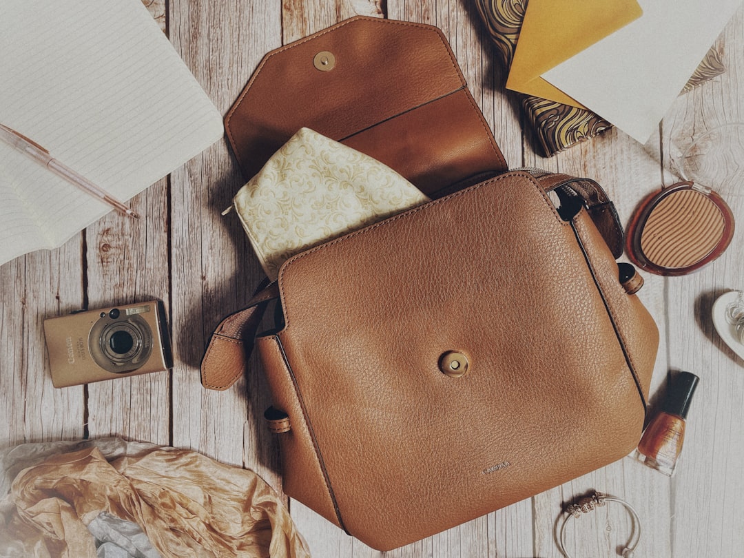 Brown leather handbag on wooden floor with camera, notebooks, and accessories scattered around