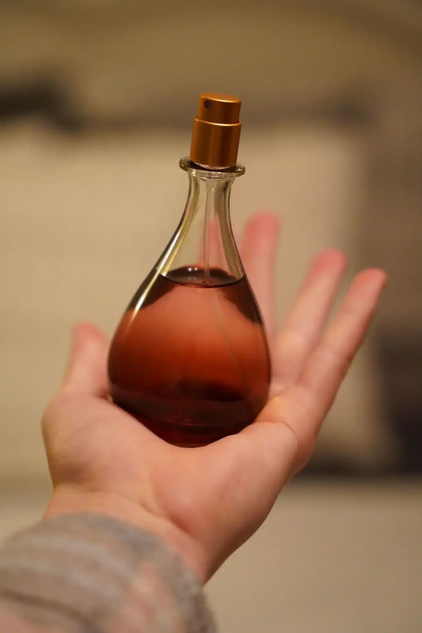 Hand holding an elegant glass perfume bottle with copper sprayer in soft lighting