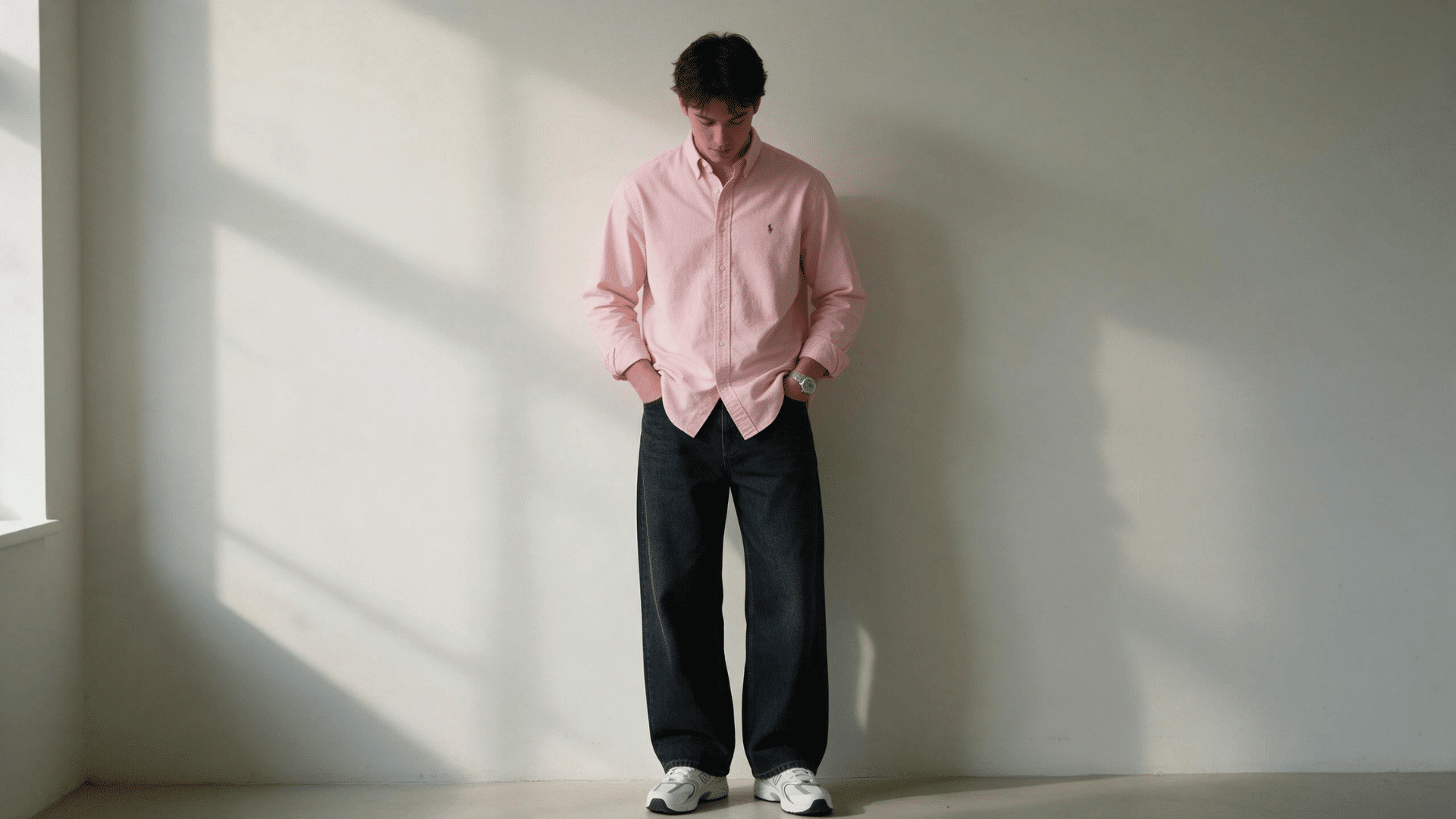 man wearing a pink button-down shirt with dark wide-leg jeans and white sneakers in natural light