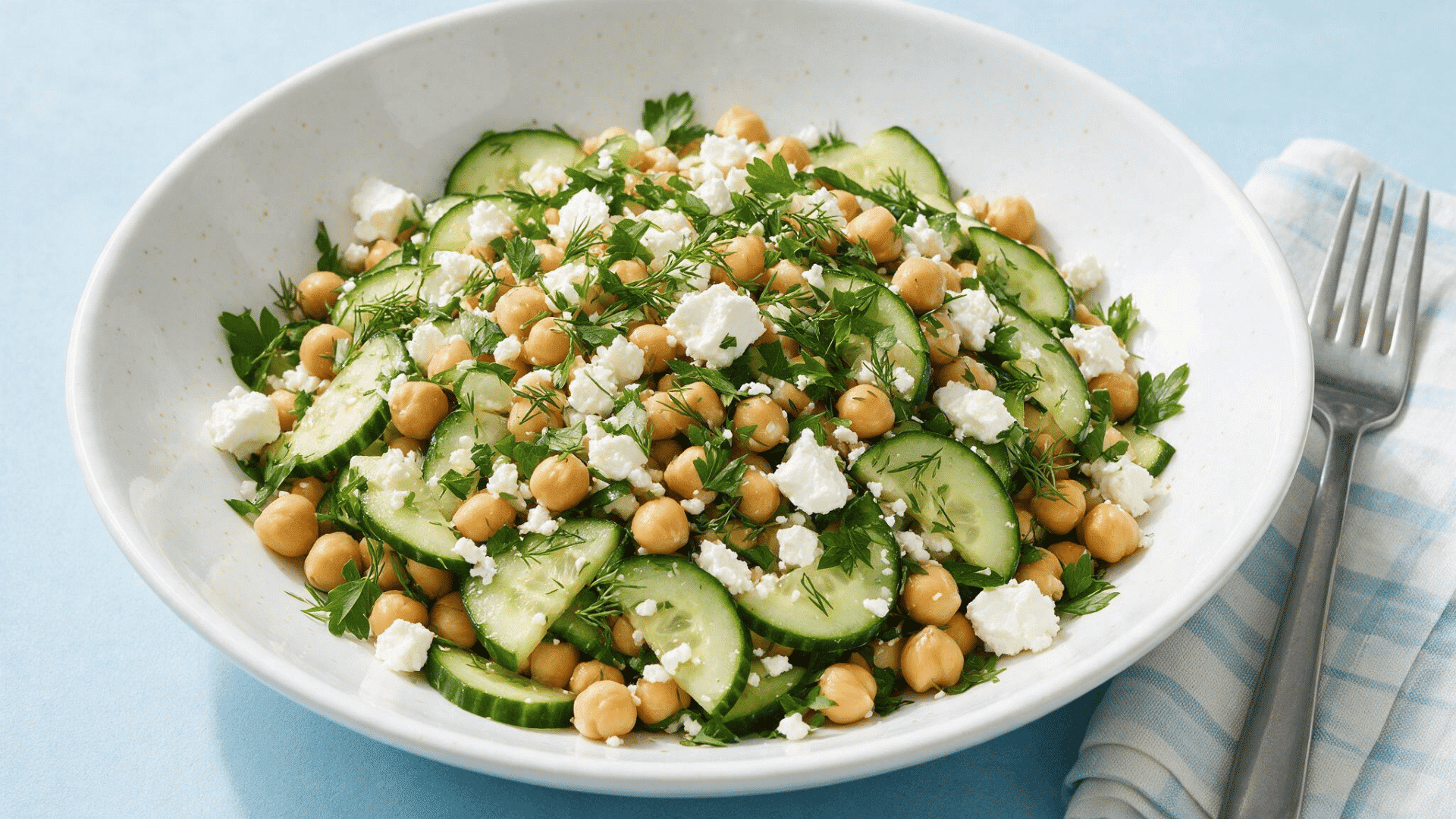 chickpea salad with cucumber, feta, parsley, and dill in a white bowl