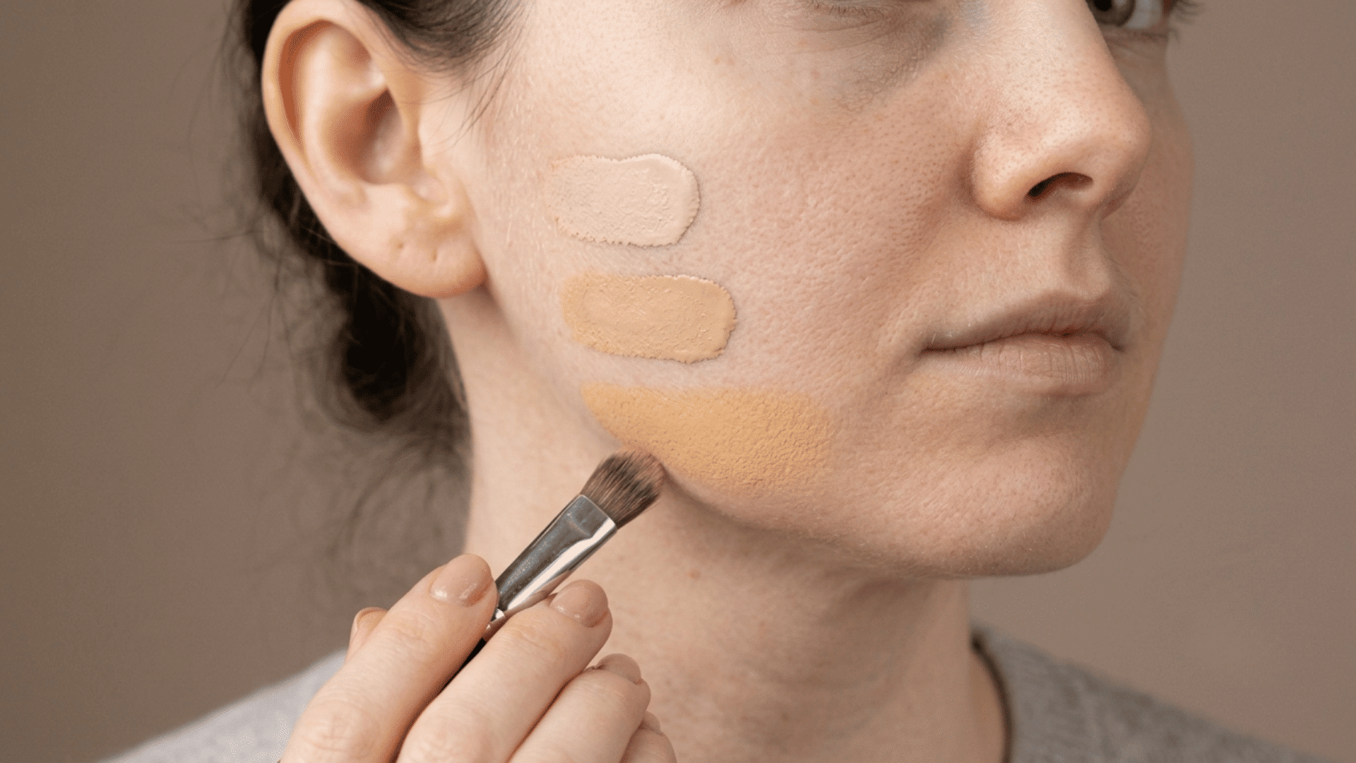 woman testing three foundation shades along her cheek and jawline with a makeup brush