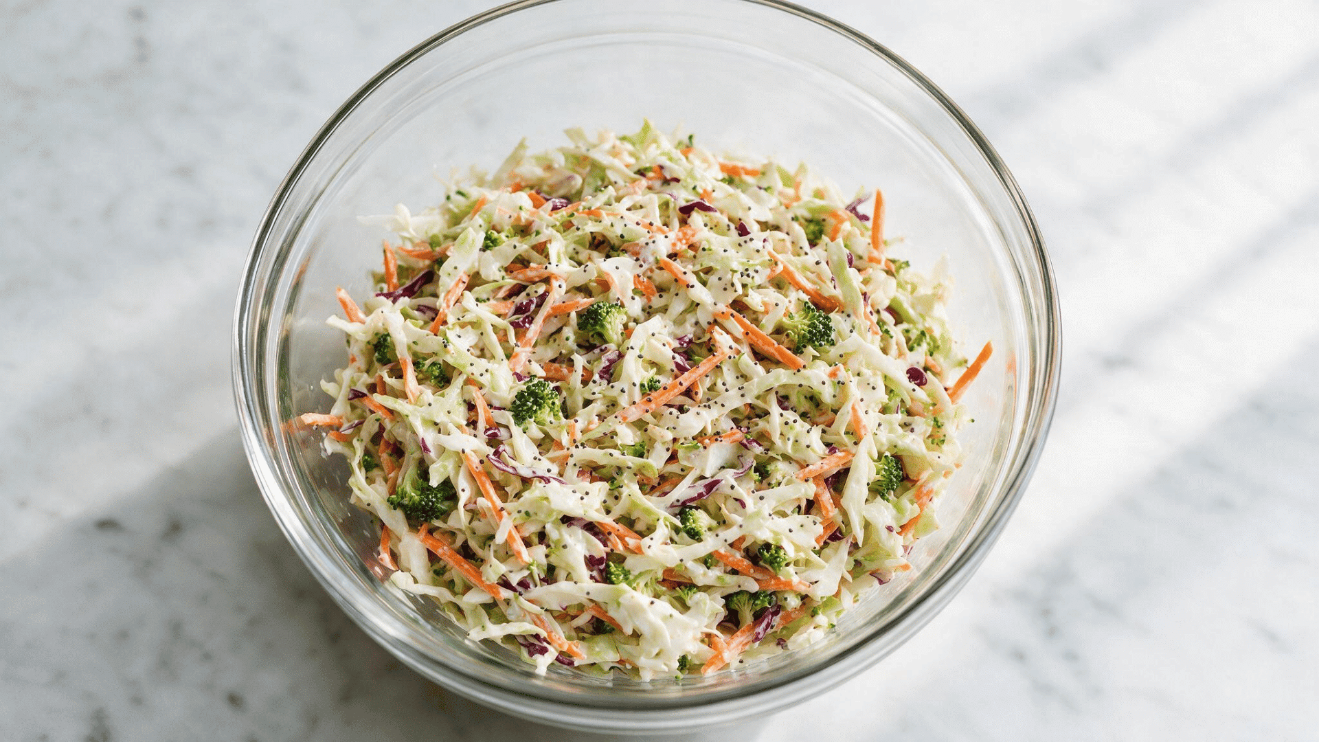 roccoli slaw with cabbage, carrots, and poppy seed dressing in a glass bowl
