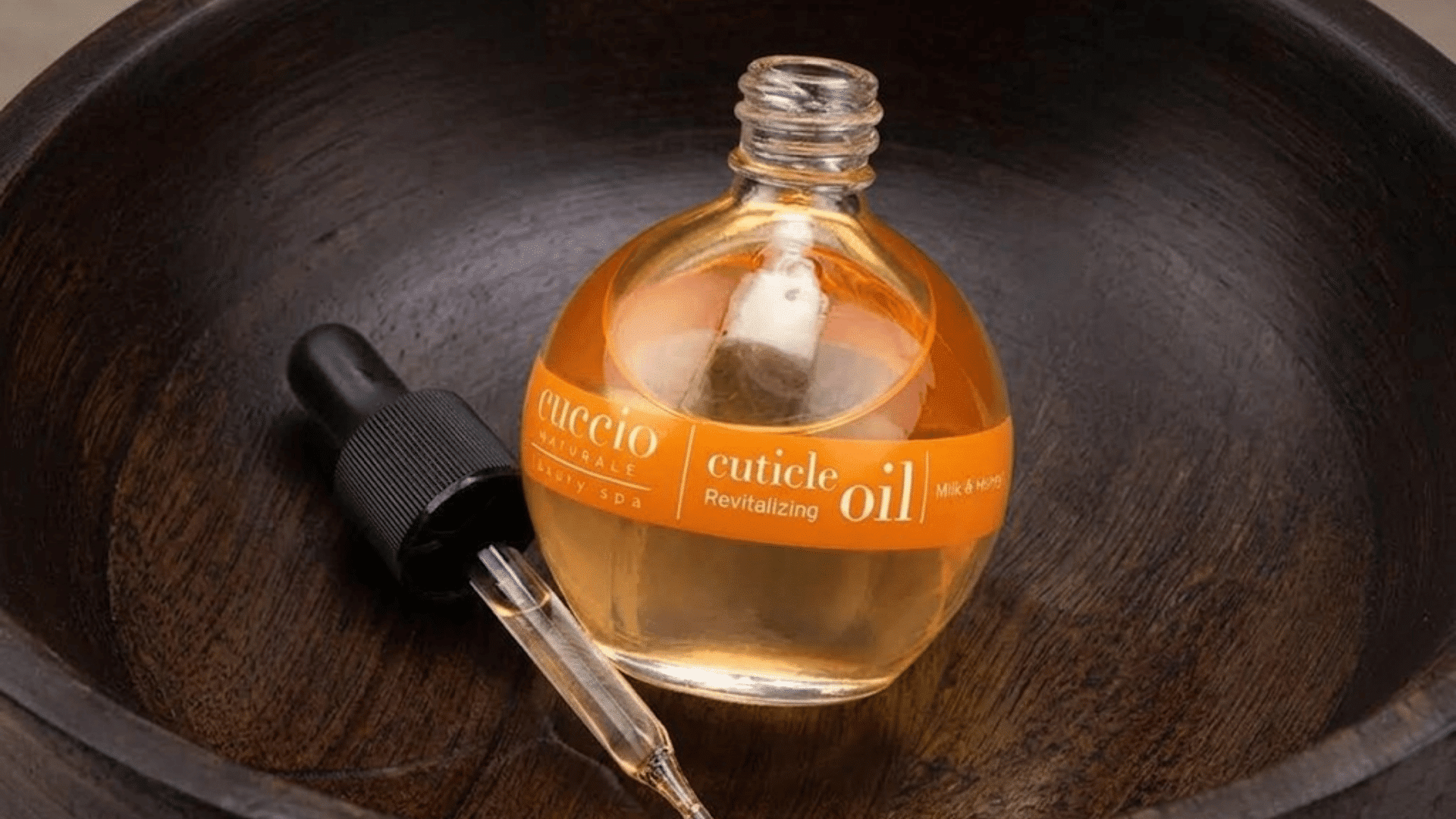 open bottle of golden cuticle oil with a glass dropper resting on a dark wooden tray