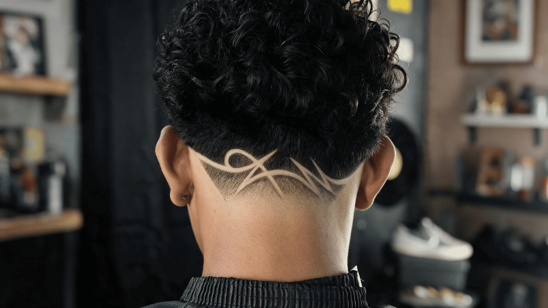 back view of curly hair with a low fade and detailed freestyle shaved design across the nape