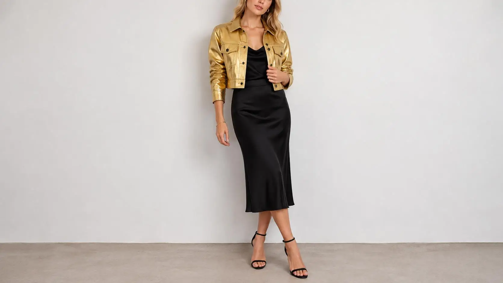 Woman in black dress and gold jacket standing against plain wall