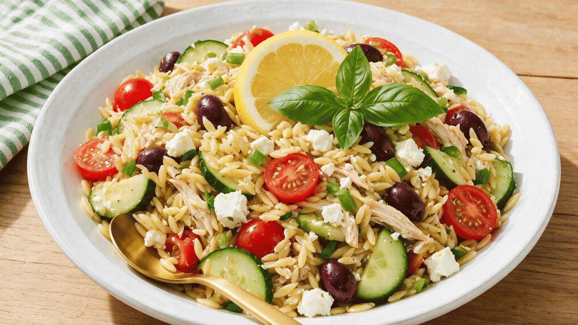 reek orzo salad with chicken, tomatoes, cucumber, olives, feta, and lemon in a bowl