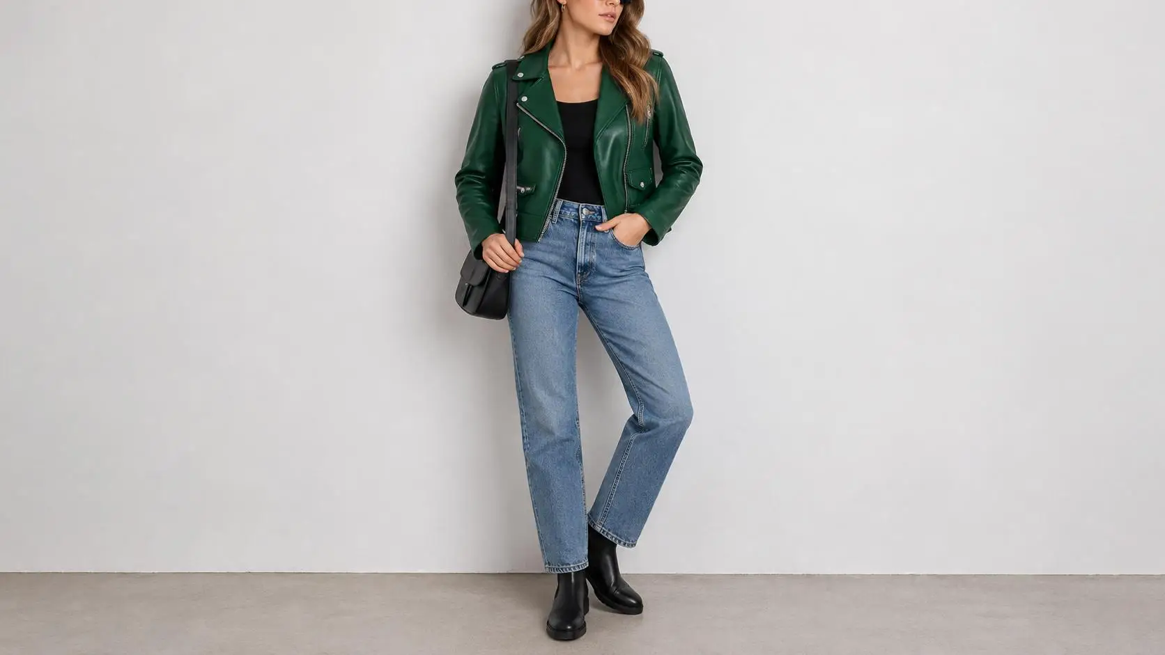 Woman in green leather jacket and jeans posing against plain wall