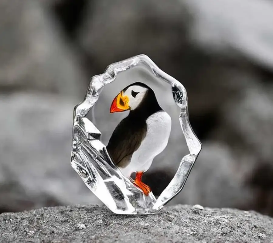 Glass sculpture of puffin resting on gray rocks with soft focus background