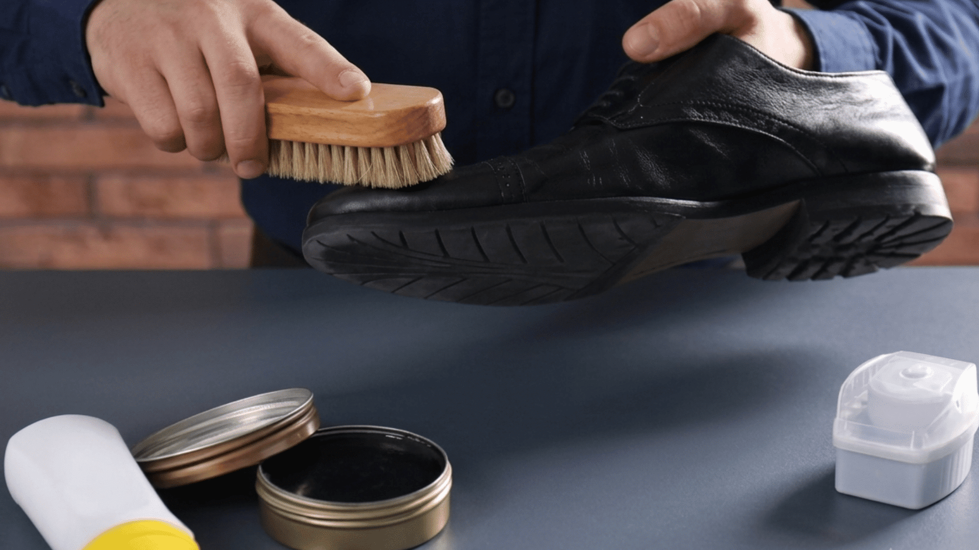person brushing black leather shoes with a soft brush and shoe polish on a table during cleaning